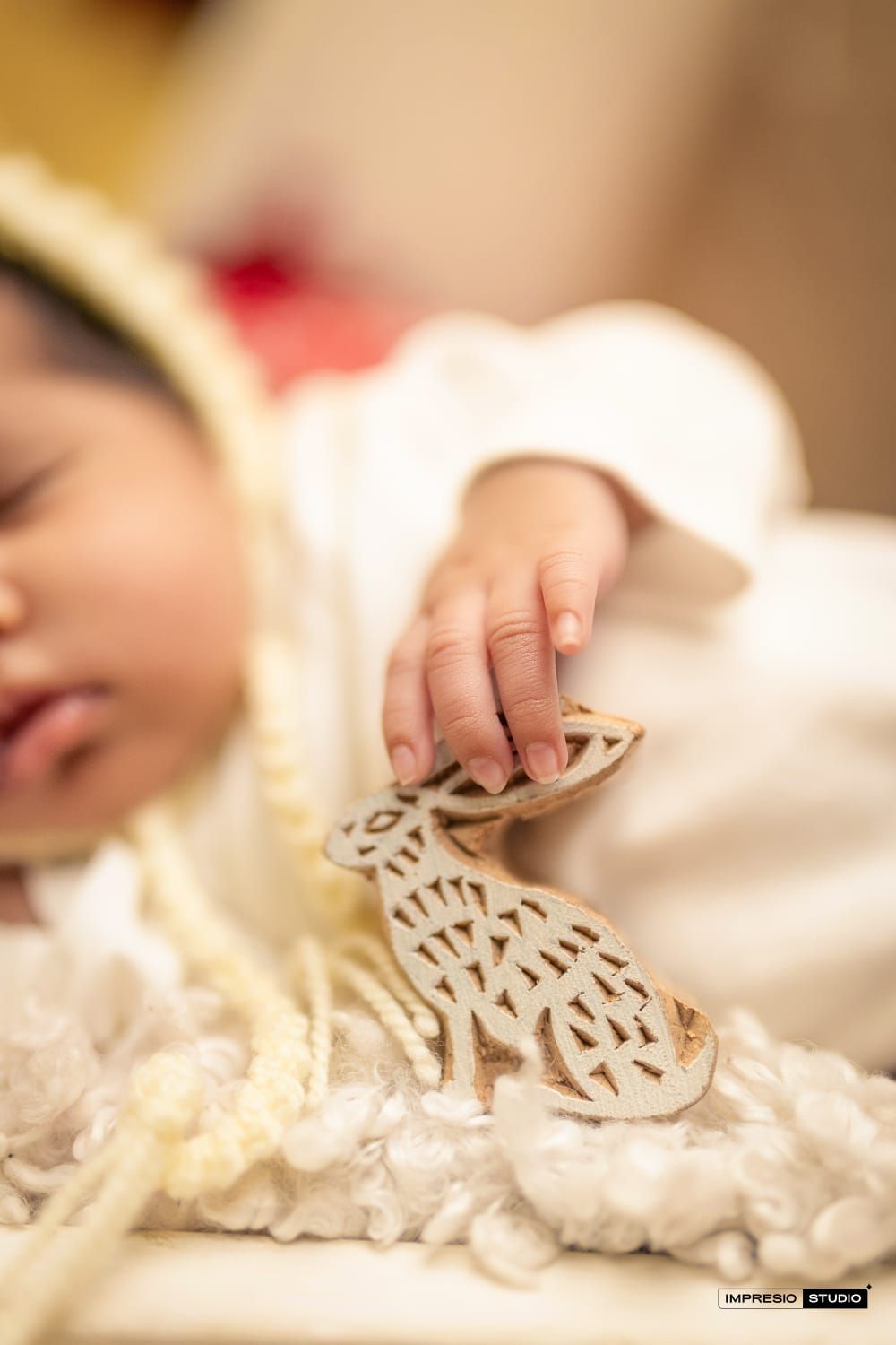 Sleeping baby in white outfit gently holding a decorative wooden block stamp with intricate animal cutout design.