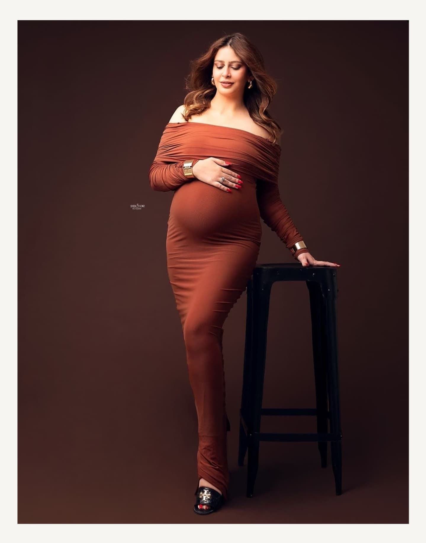 Maternity photo series in rust-colored dress against dark background.