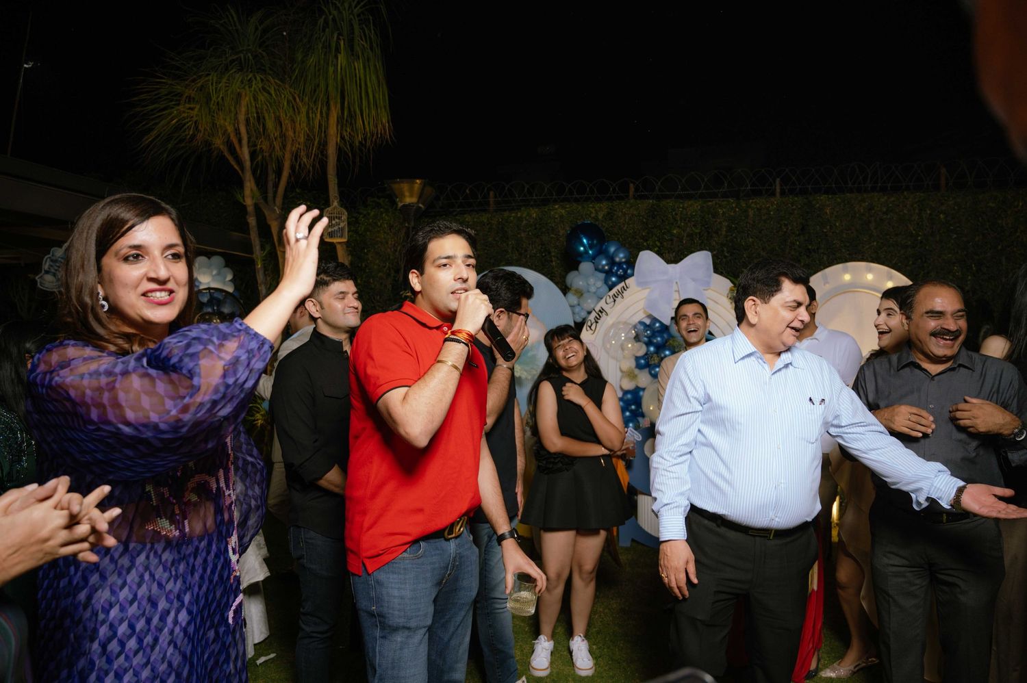 Group of people celebrating at an outdoor night party, with a man singing into a microphone on a festive occasion.