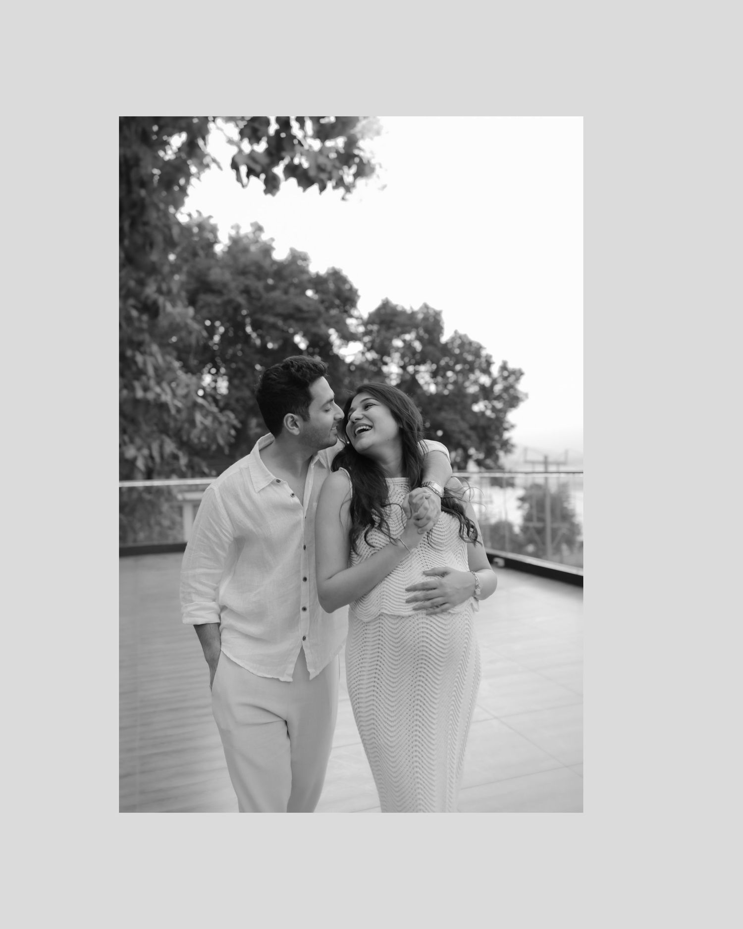 A romantic couple in white outfits share an intimate moment together on a balcony in black and white photography.