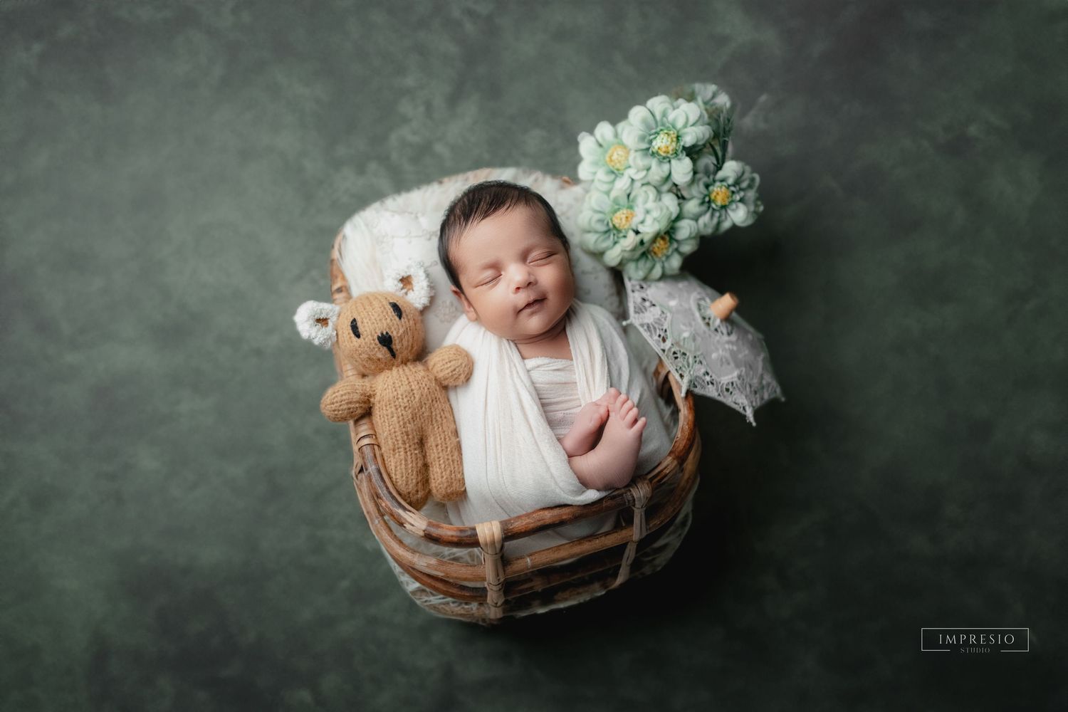 Black and white newborn photography series on a dark background with baskets and teddy bear props.