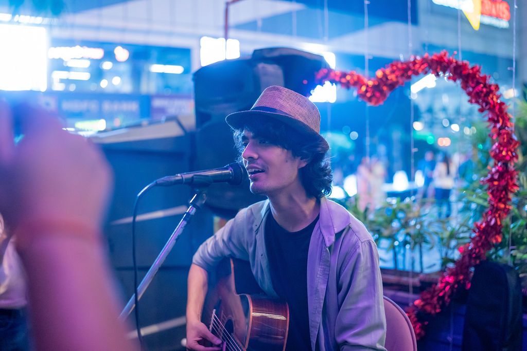 Young male musician playing acoustic guitar and singing into a microphone at an outdoor venue at night.
