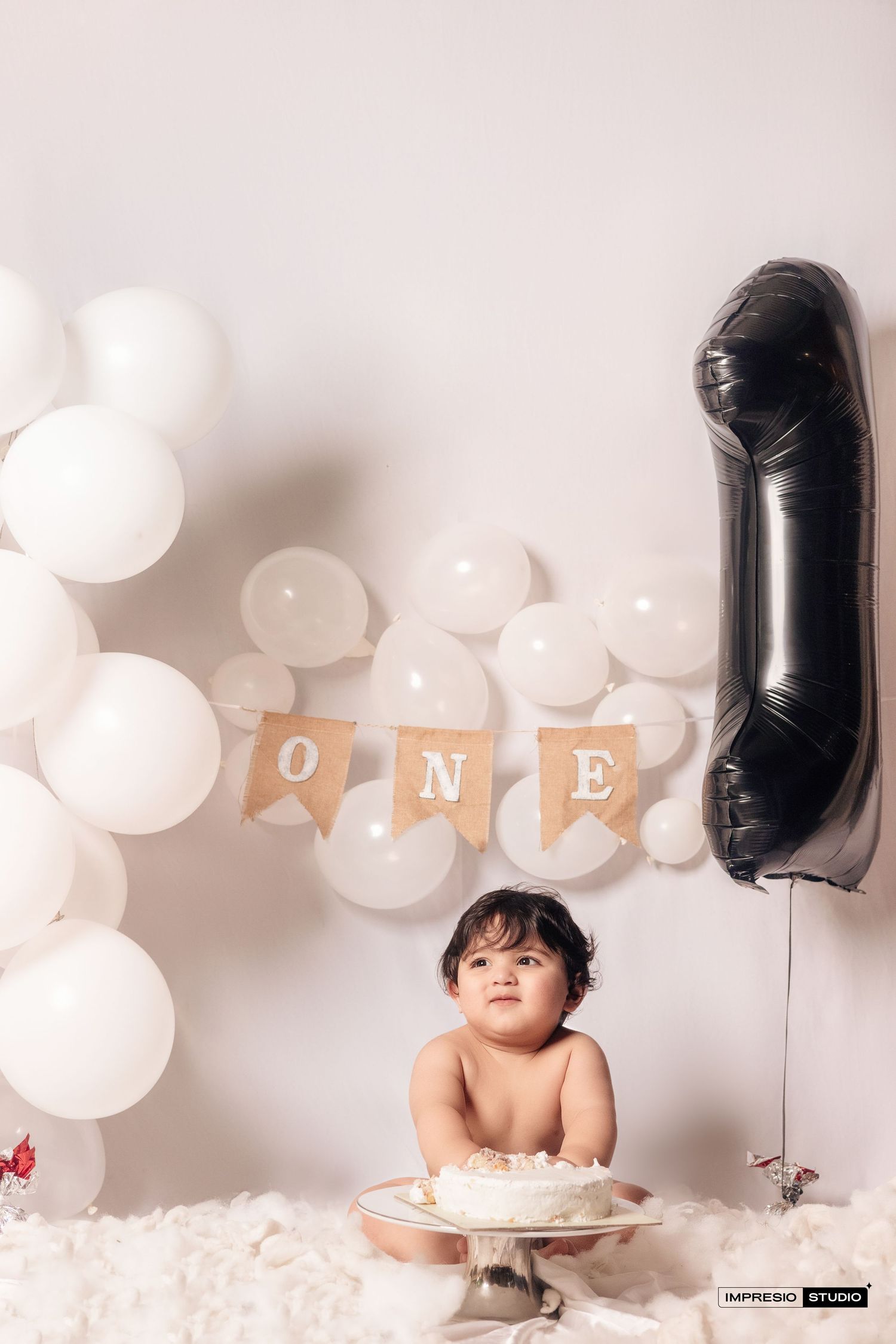 A festive first birthday setup with white and black balloons arranged in a row against a light background.