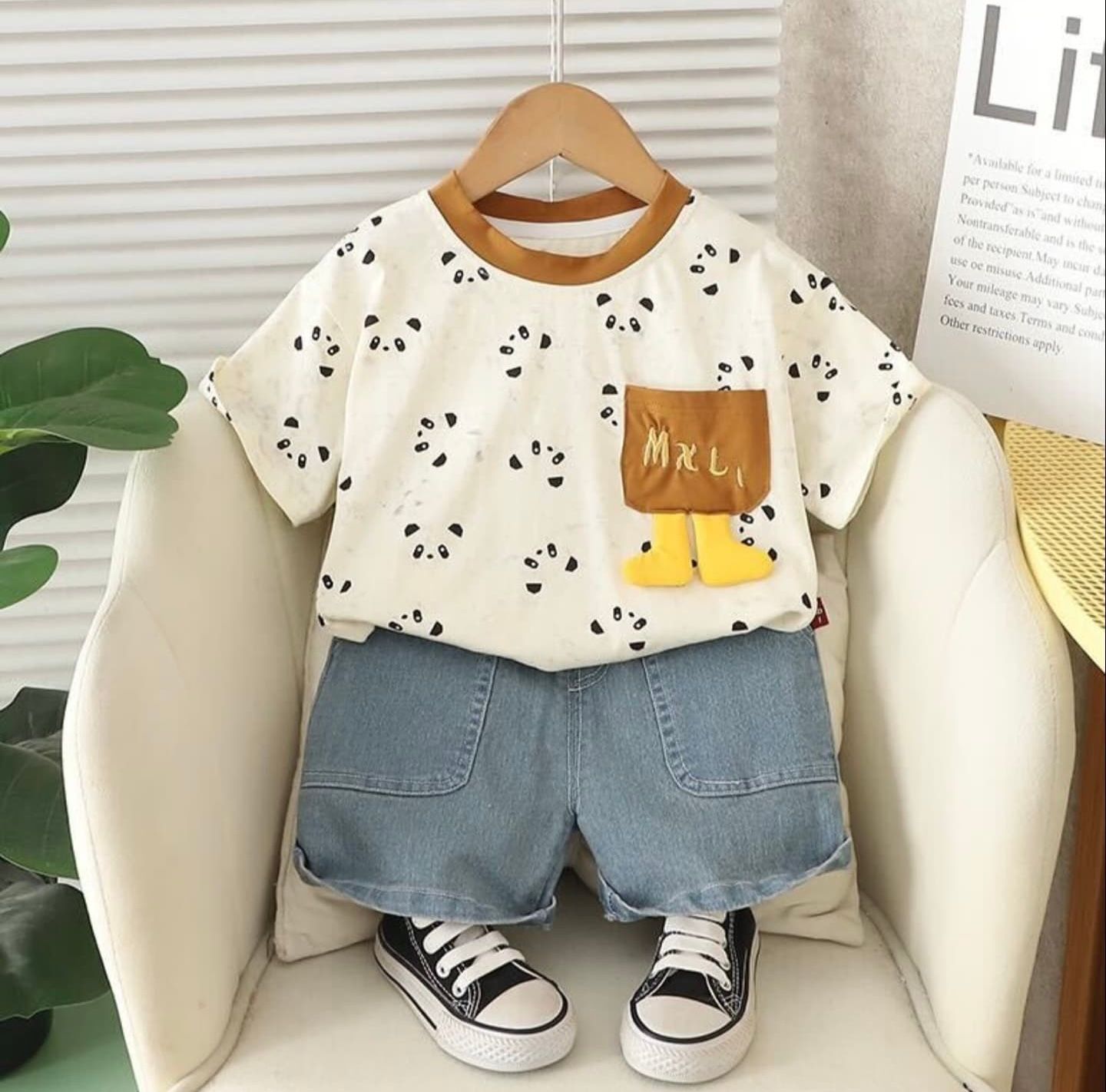 Cute children's outfit with panda print t-shirt, brown pocket accent, denim shorts and black sneakers displayed on hanger.