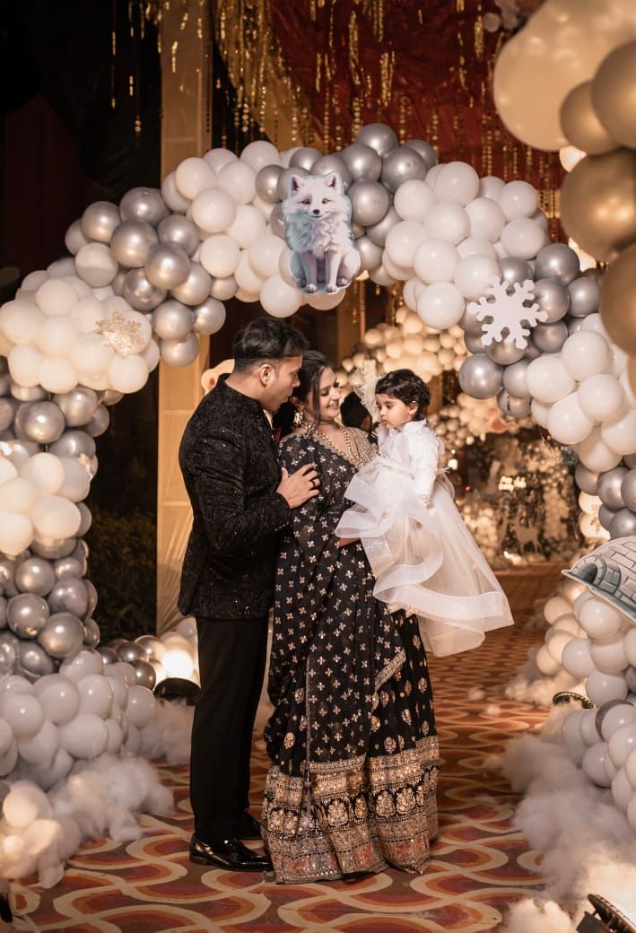 Family poses under elegant silver and white balloon arch with snowflake decor at a festive celebration event.
