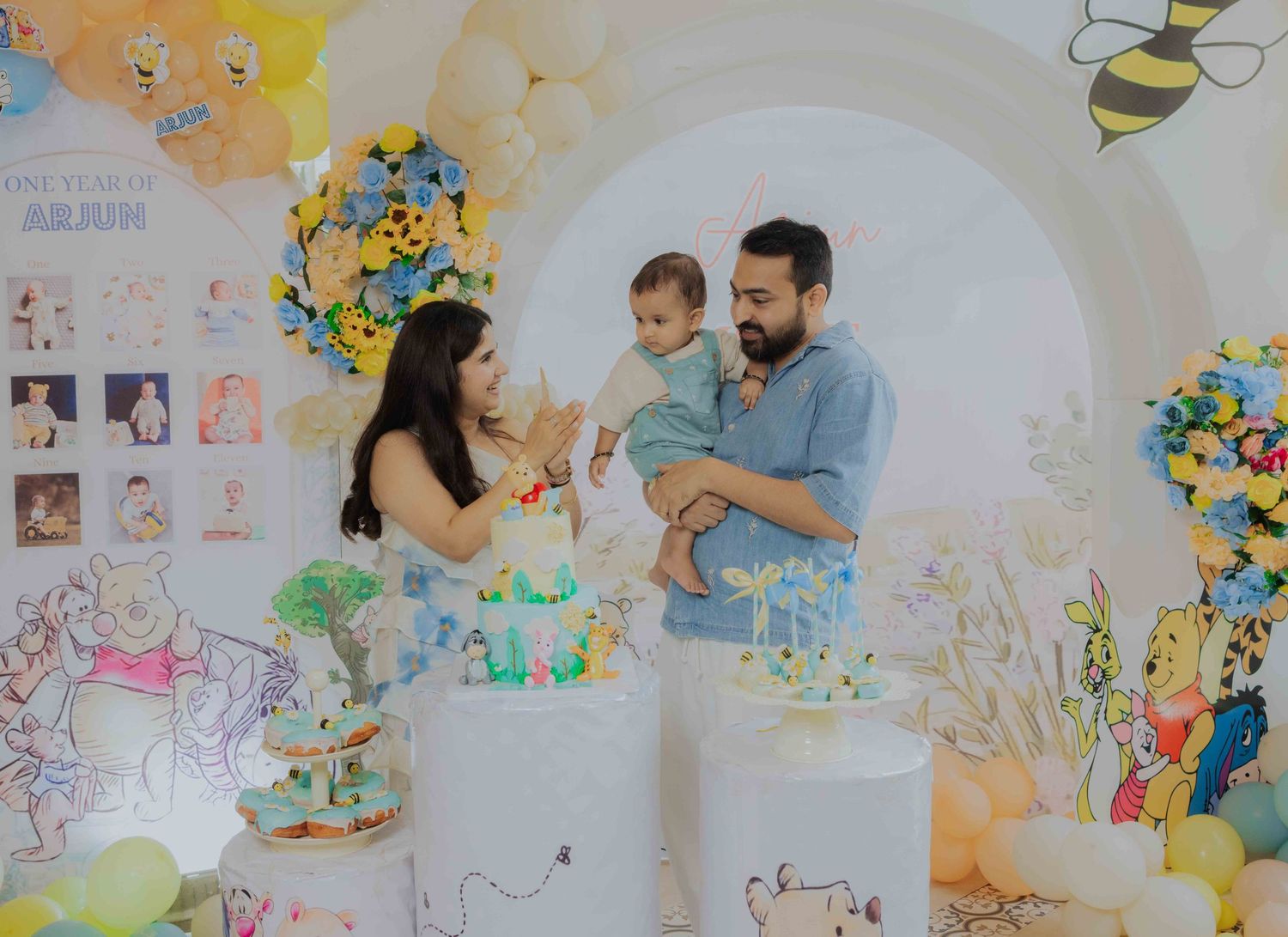 Family celebrating baby's first birthday with Winnie the Pooh themed decorations, balloons, and cake.