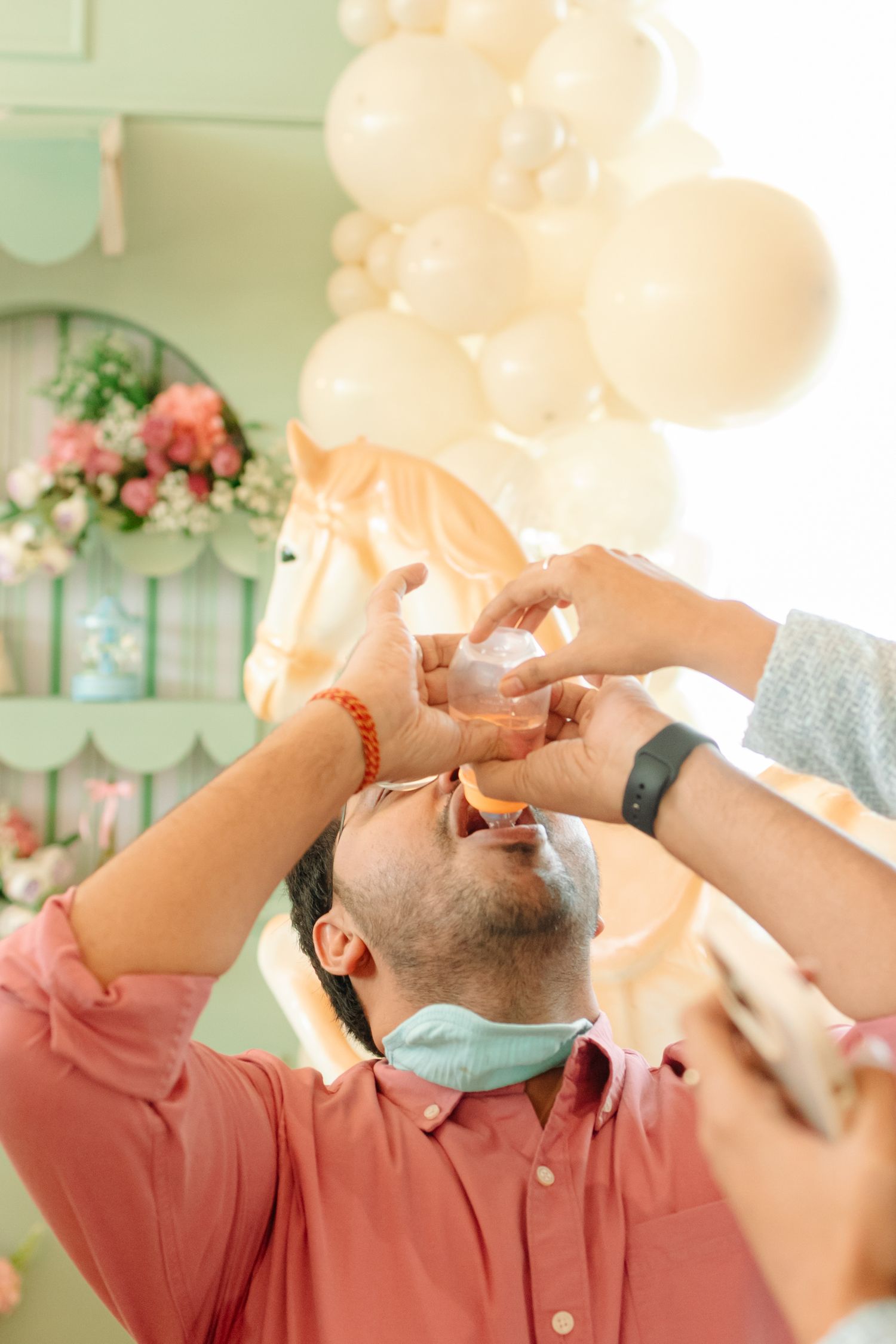 Man having cake smashed into his face at a pastel party with balloon garland and floral decorations.