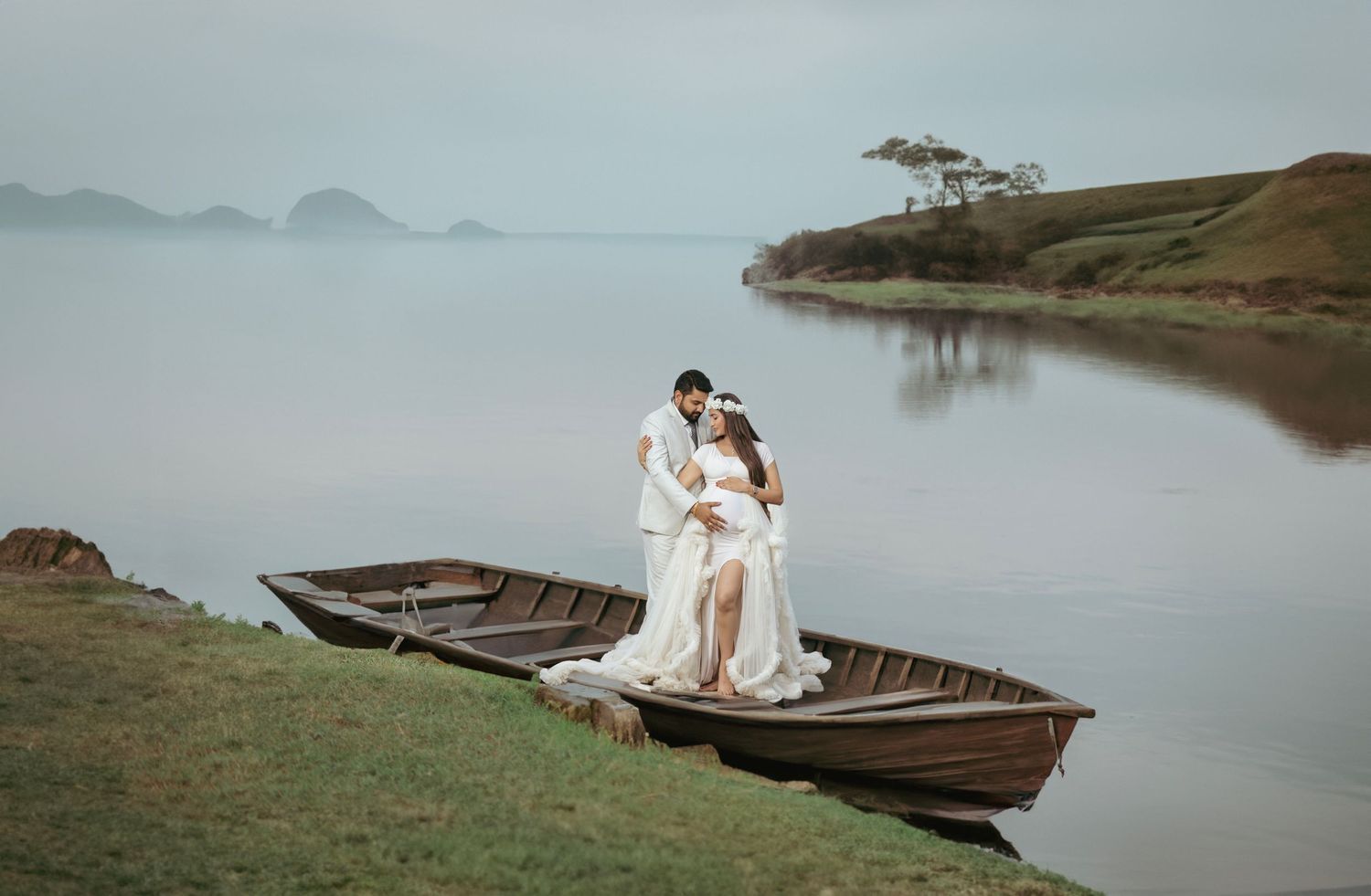 Romantic lakeside maternity photos featuring a wooden boat and misty water views.