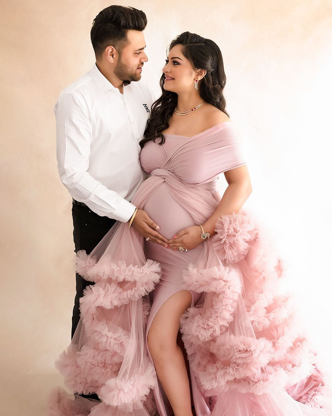 An intimate maternity studio portrait featuring a pink ruffled gown.