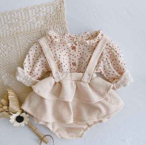 Delicate floral print baby romper with corduroy suspender skirt in cream color.