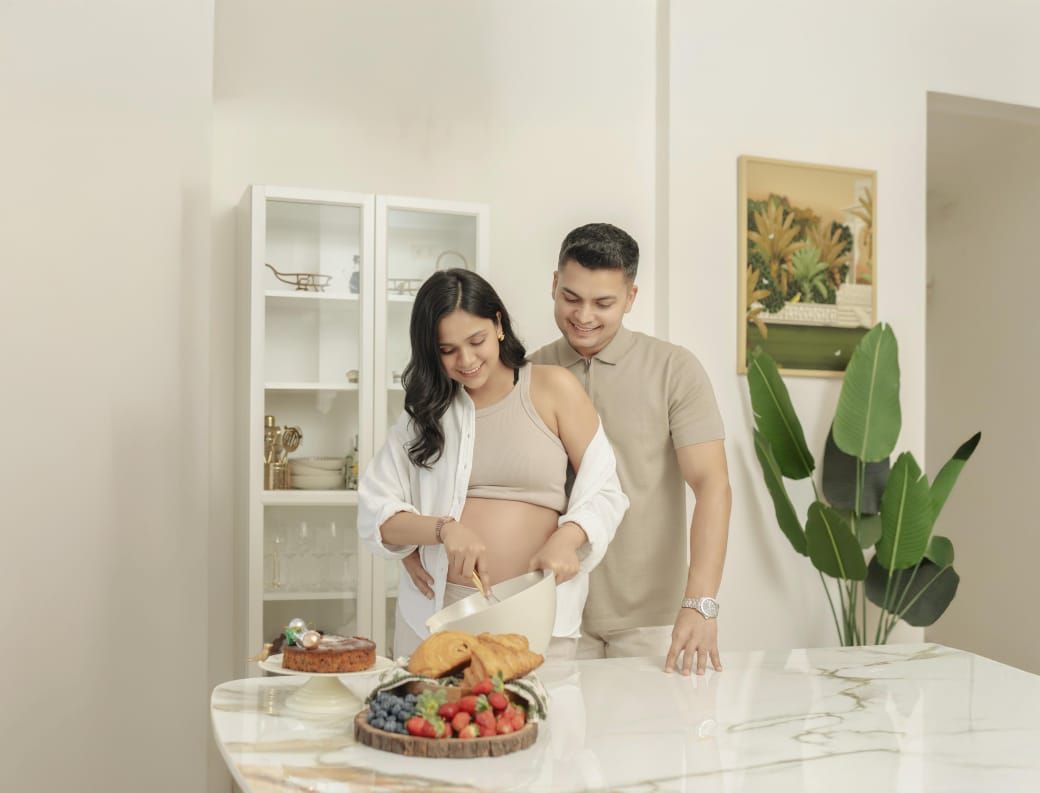 Couple preparing healthy breakfast together in modern white kitchen with tropical plant decor for maternity photography.