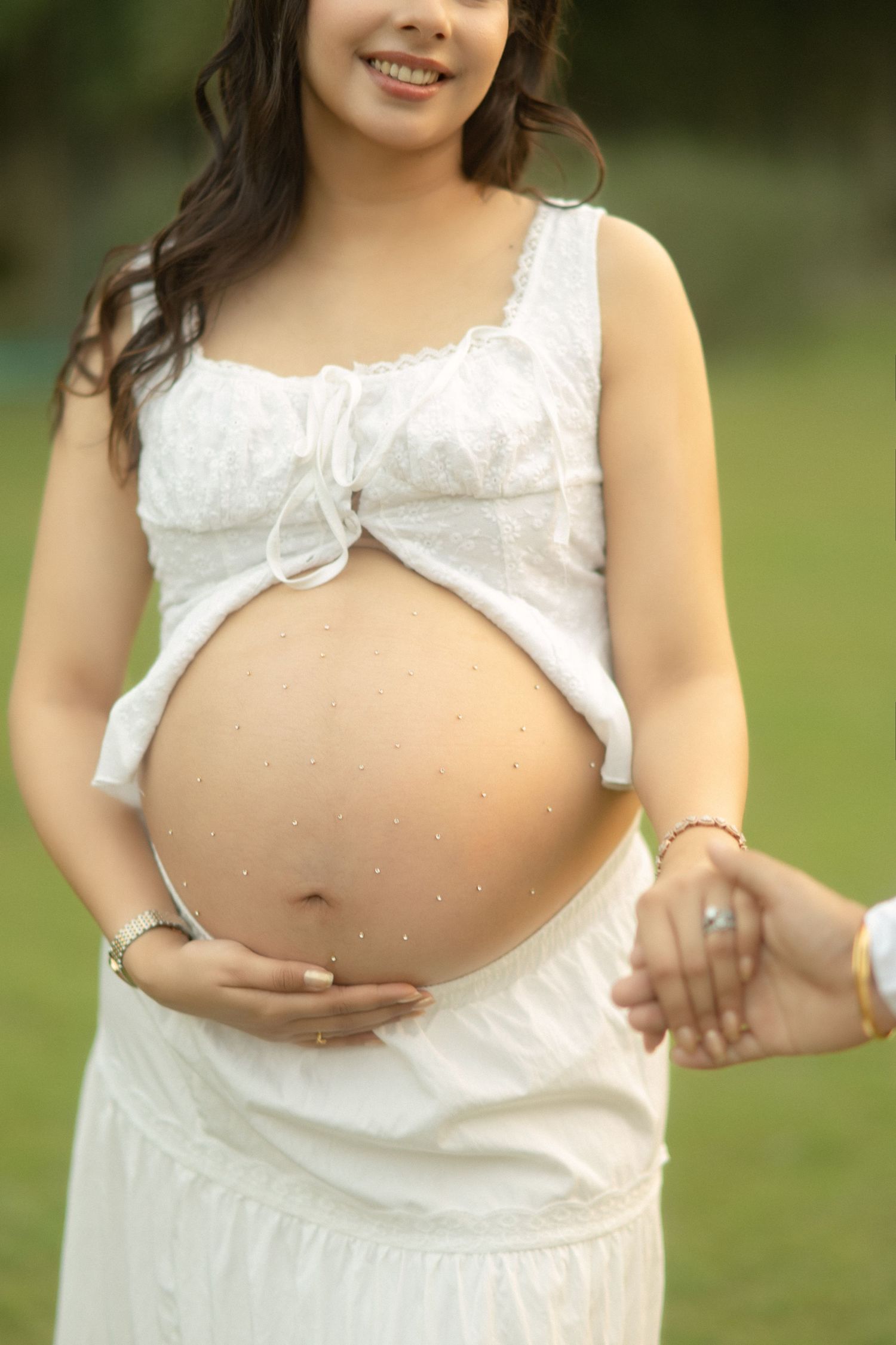 A maternity photo series shows a woman in a white dress posing outdoors on a grassy lawn.