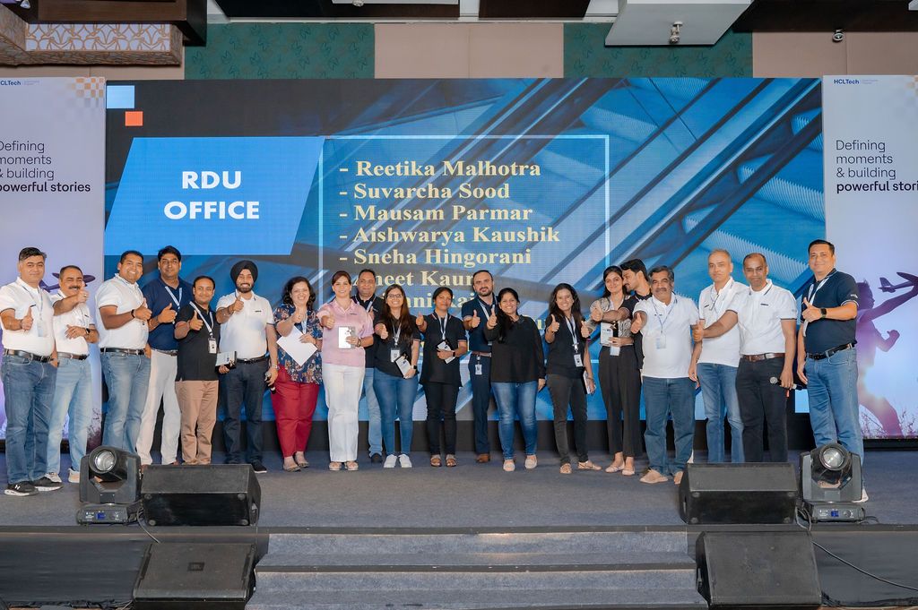 A large group of people standing together at a corporate event with blue backdrop displays and banners.
