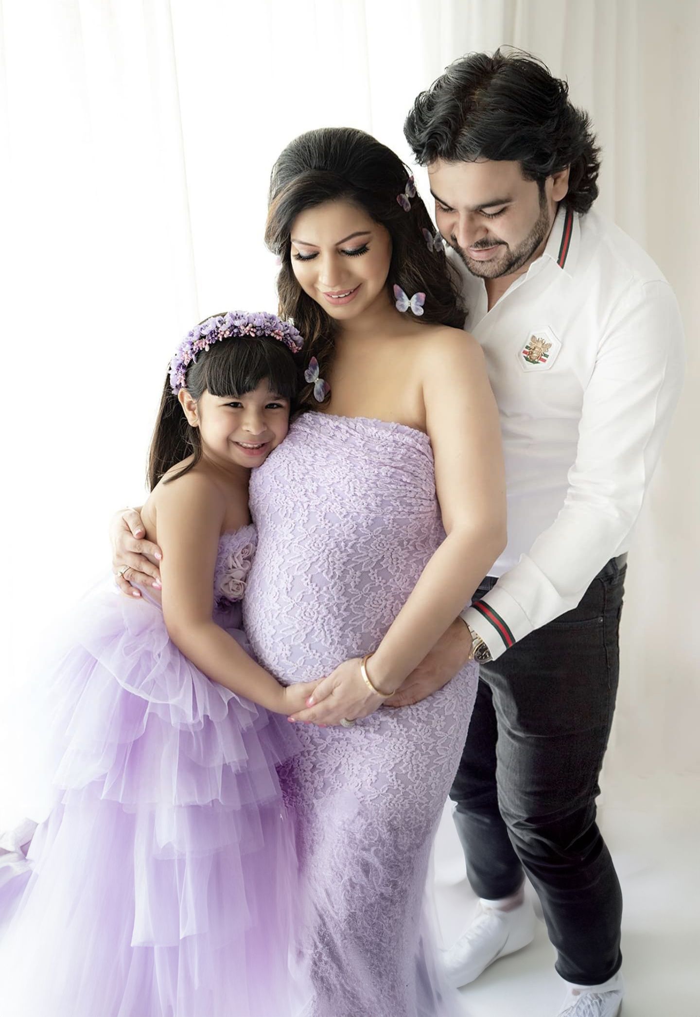 A heartwarming maternity photo series showing tender family moments in a white studio setting with lavender dresses.