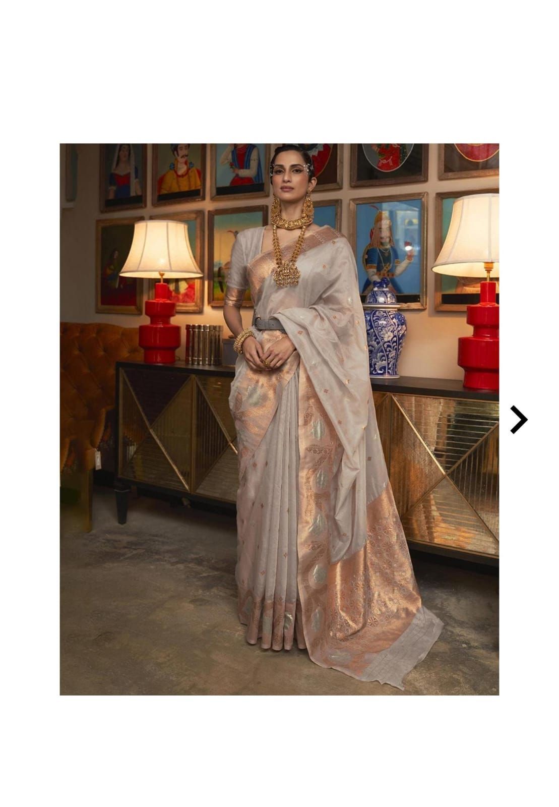 Beige and gold silk saree displayed in an elegant indoor setting with decorative elements.