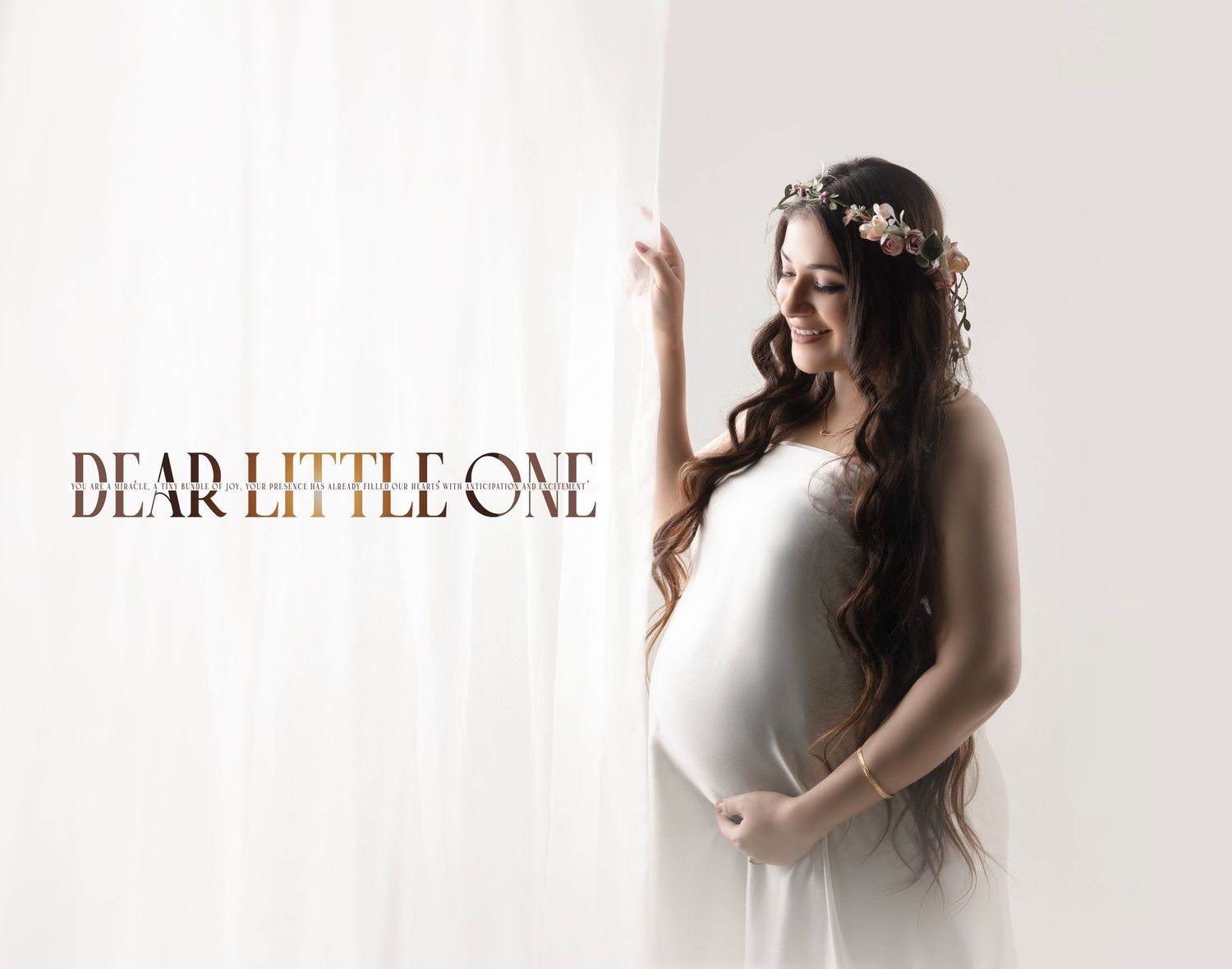 Ethereal maternity portrait in white dress with floral crown against light background.