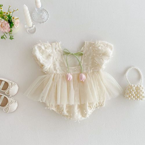 Delicate cream lace baby romper dress with tulle skirt displayed with matching shoes and pearl handbag.