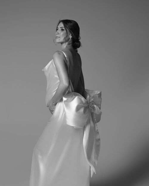 Black and white portrait of an elegant wedding dress with a dramatic oversized bow detail on the back.
