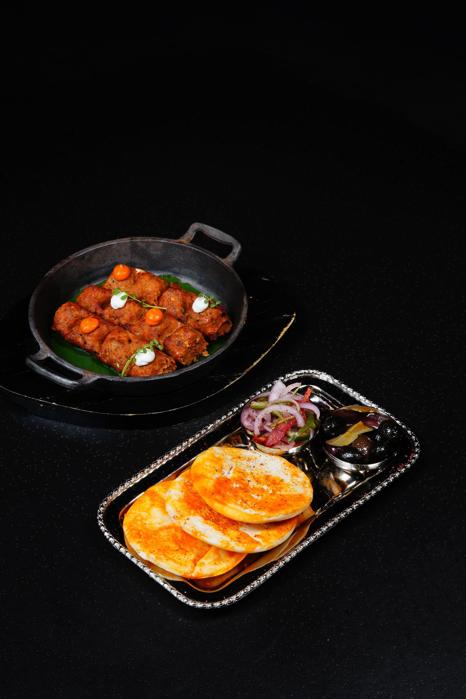 Spicy Indian meatballs in a black pan served with flatbreads, onion salad, and chutney on a dark background.