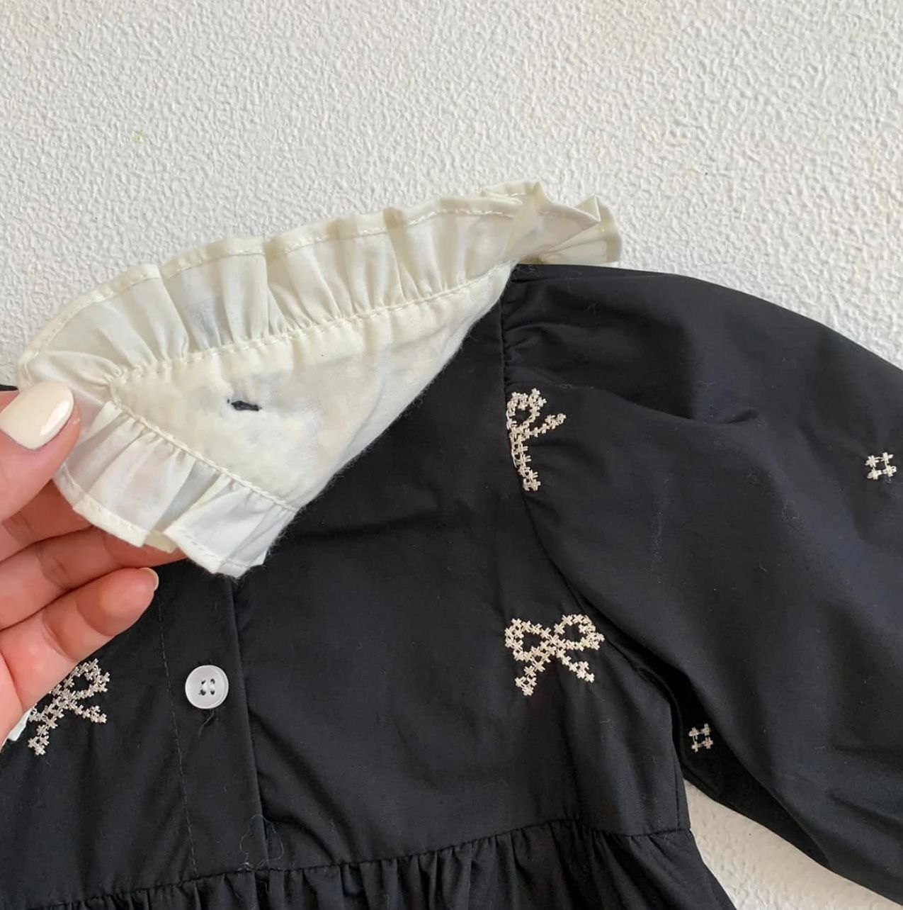 Close-up details of a black dress with white ruffled collar and sparkly rhinestone embellishments.