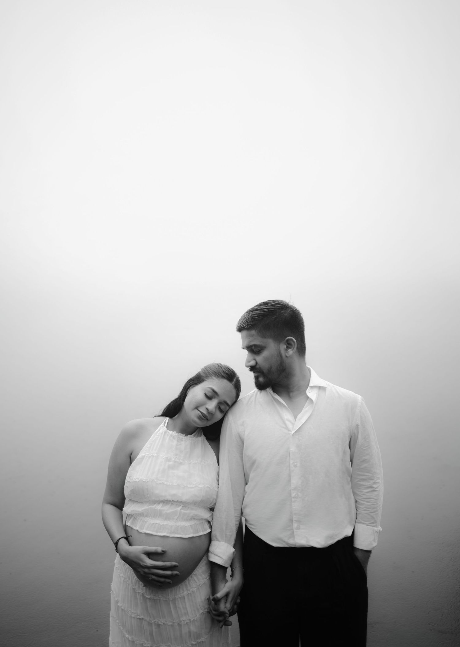 A couple in white clothing stands together in a series of intimate black and white photographs.