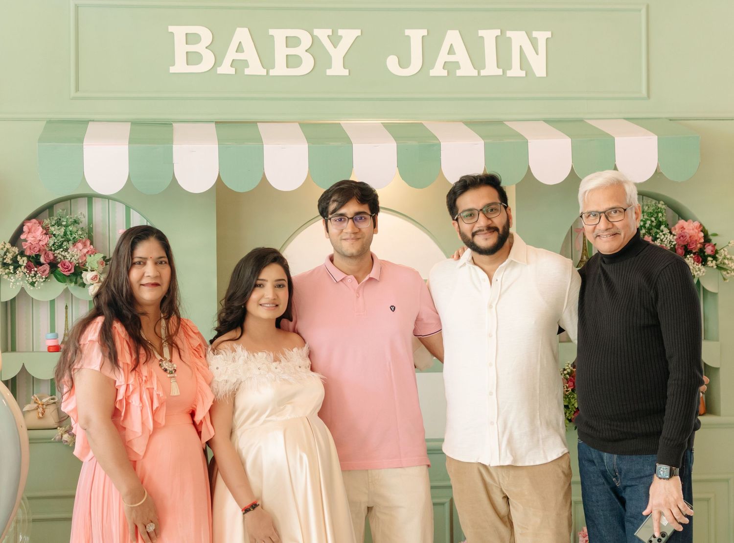 Five people pose together at a Baby Jain baby shower celebration in front of a green pastel decorated backdrop.