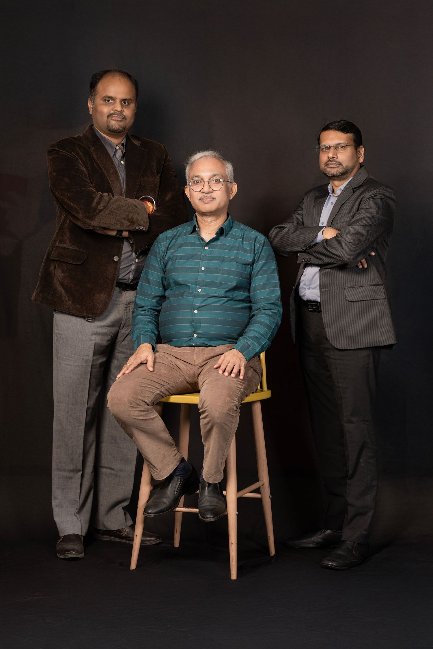 Professional studio portraits show two men in business attire against dark background, one seated and one standing.