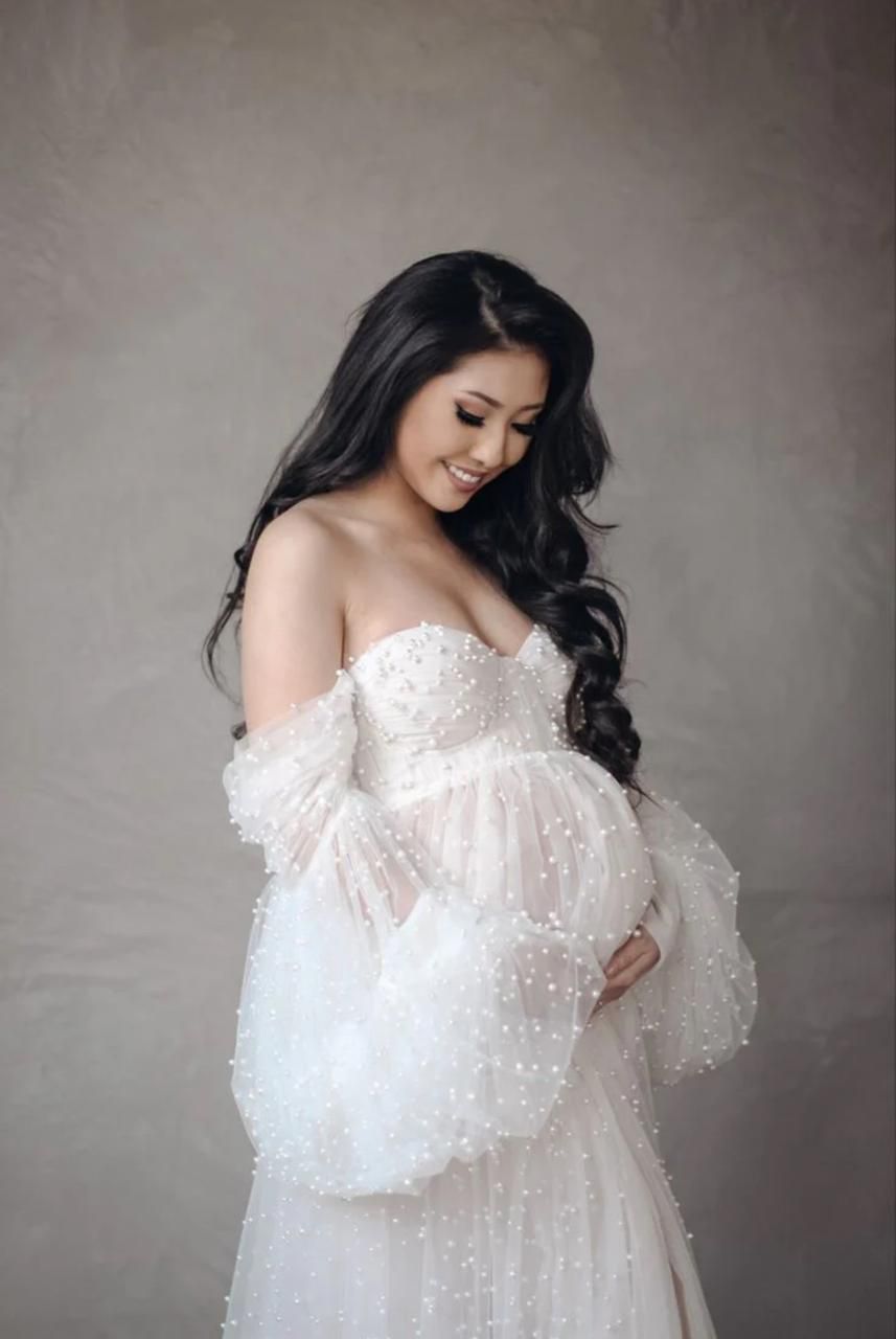 Ethereal maternity photography in a white lace off-shoulder gown against neutral backdrop.