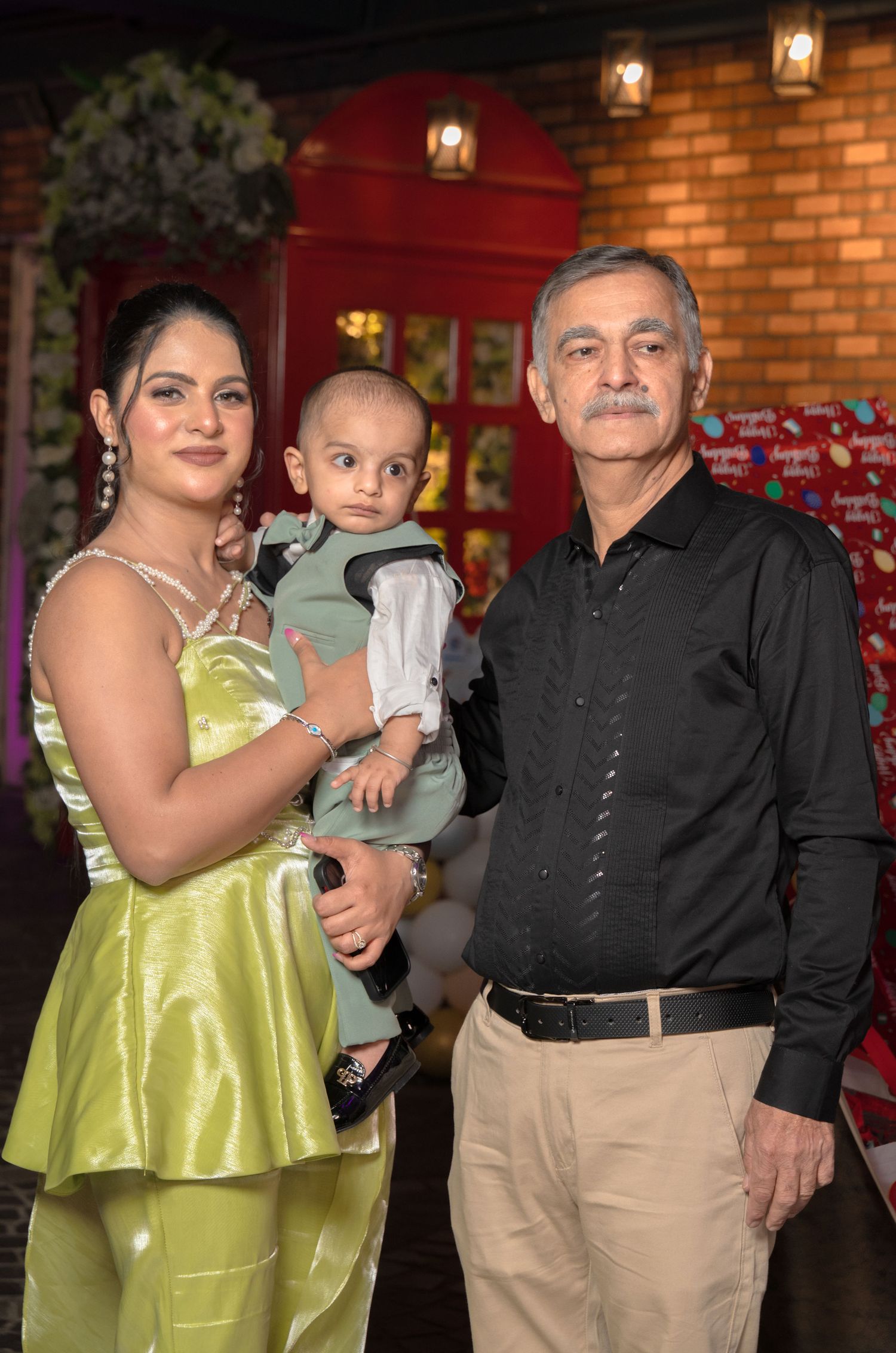 A family poses in front of a brick wall with lanterns, featuring a lime green dress and formal attire at an event.