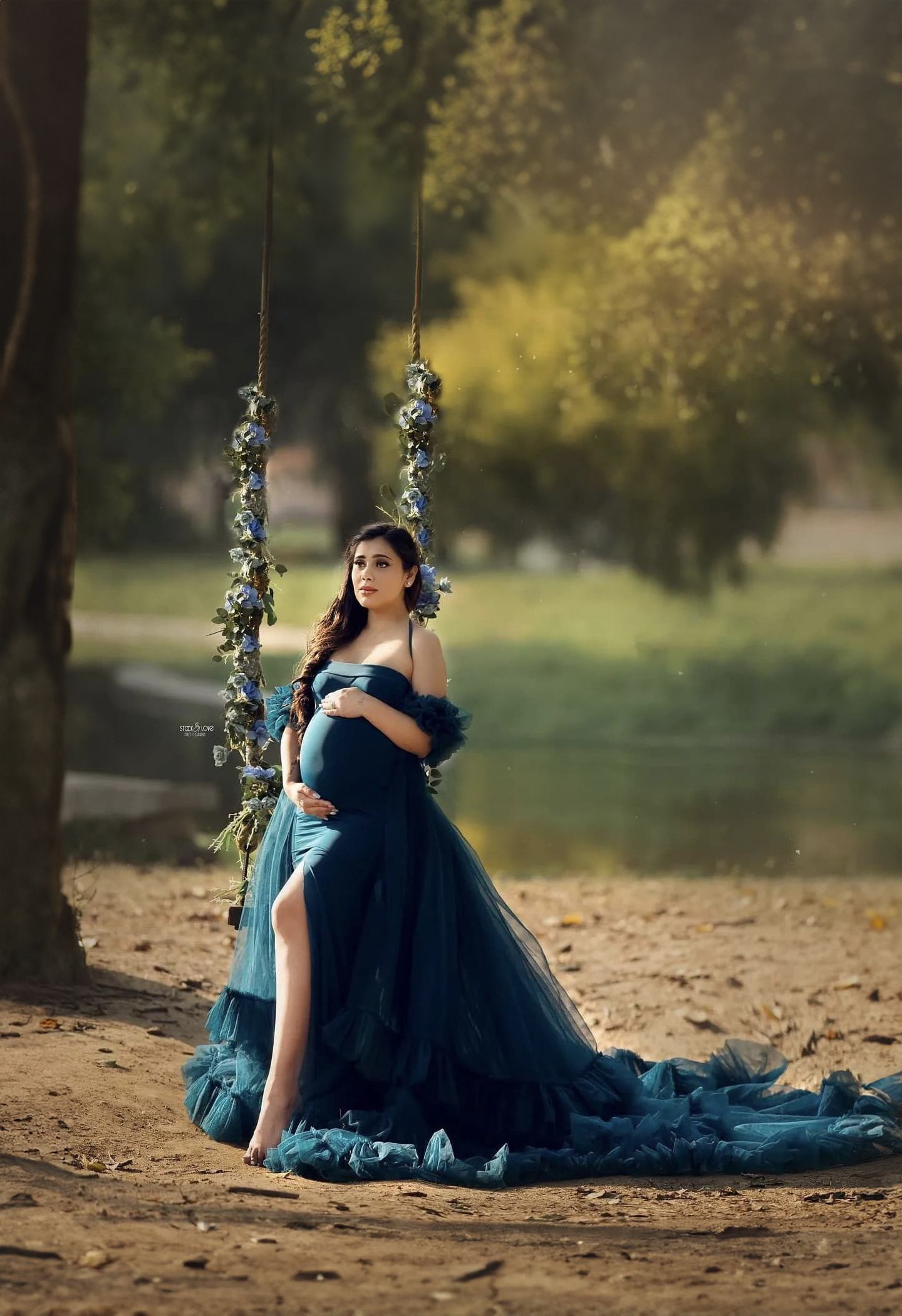 Ethereal maternity photo on a floral swing in a navy blue tulle gown with dramatic train in nature setting.