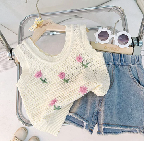 White knit top with floral embroidery paired with denim shorts on display.