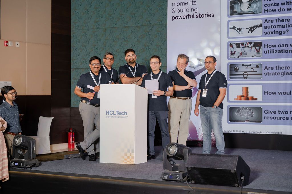 Six men stand on stage around an HCLTech podium during a corporate event, with presentation slides displayed on screens behind them.