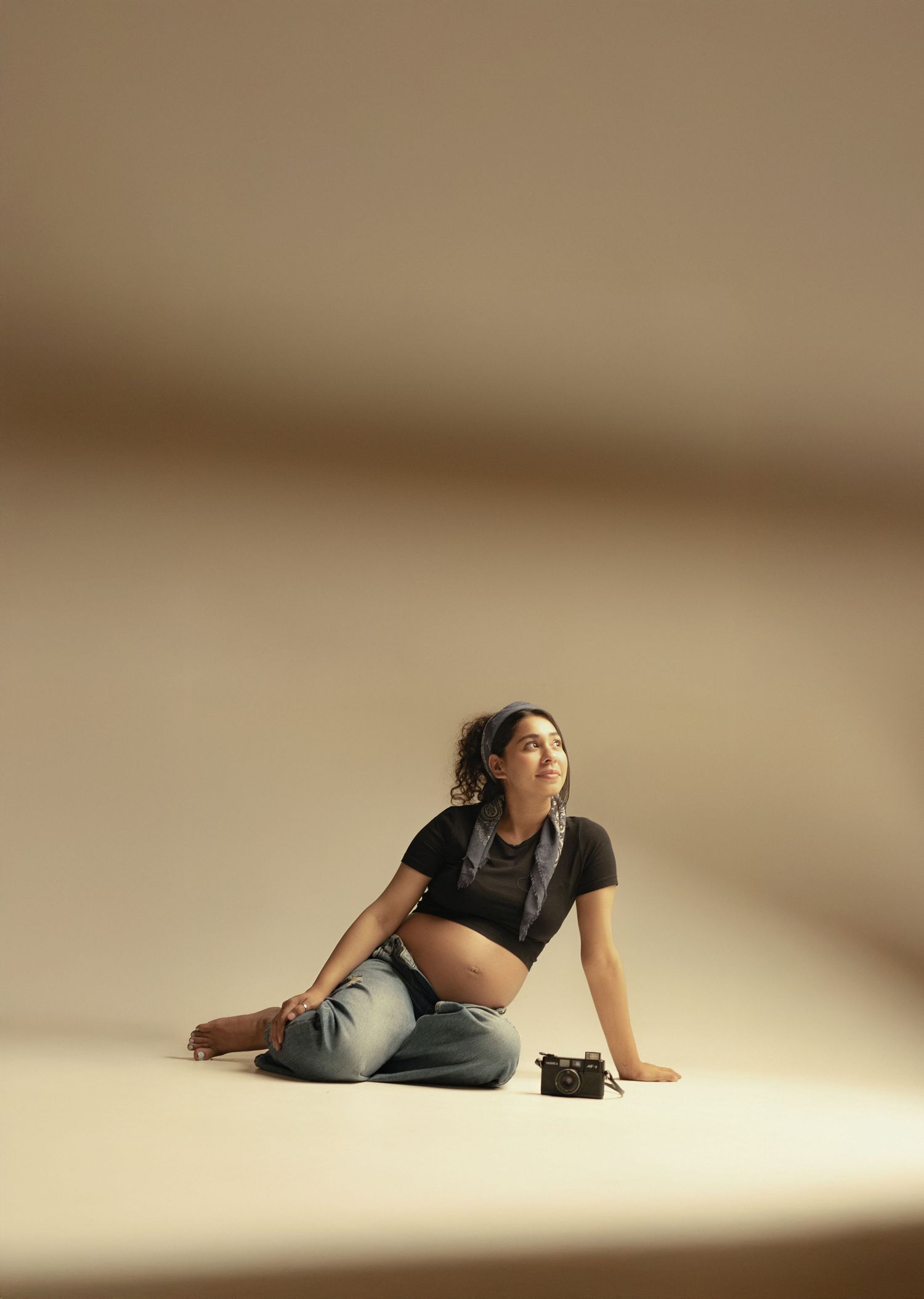 Person in casual attire lying on floor in artistic pose against neutral background with dramatic lighting.