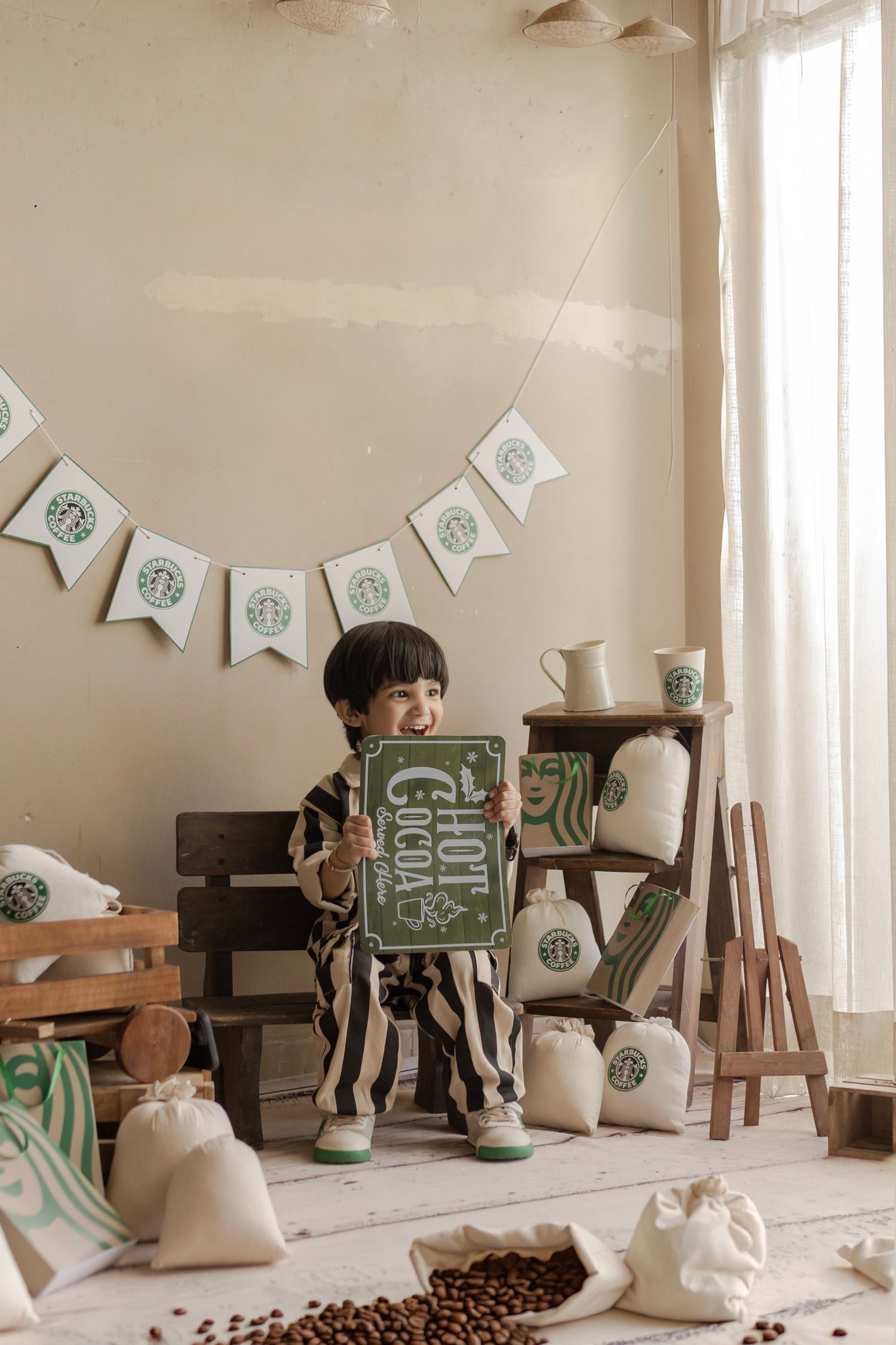 Child holding a Hot Cocoa sign in a Starbucks-themed play area with coffee beans and burlap sacks.