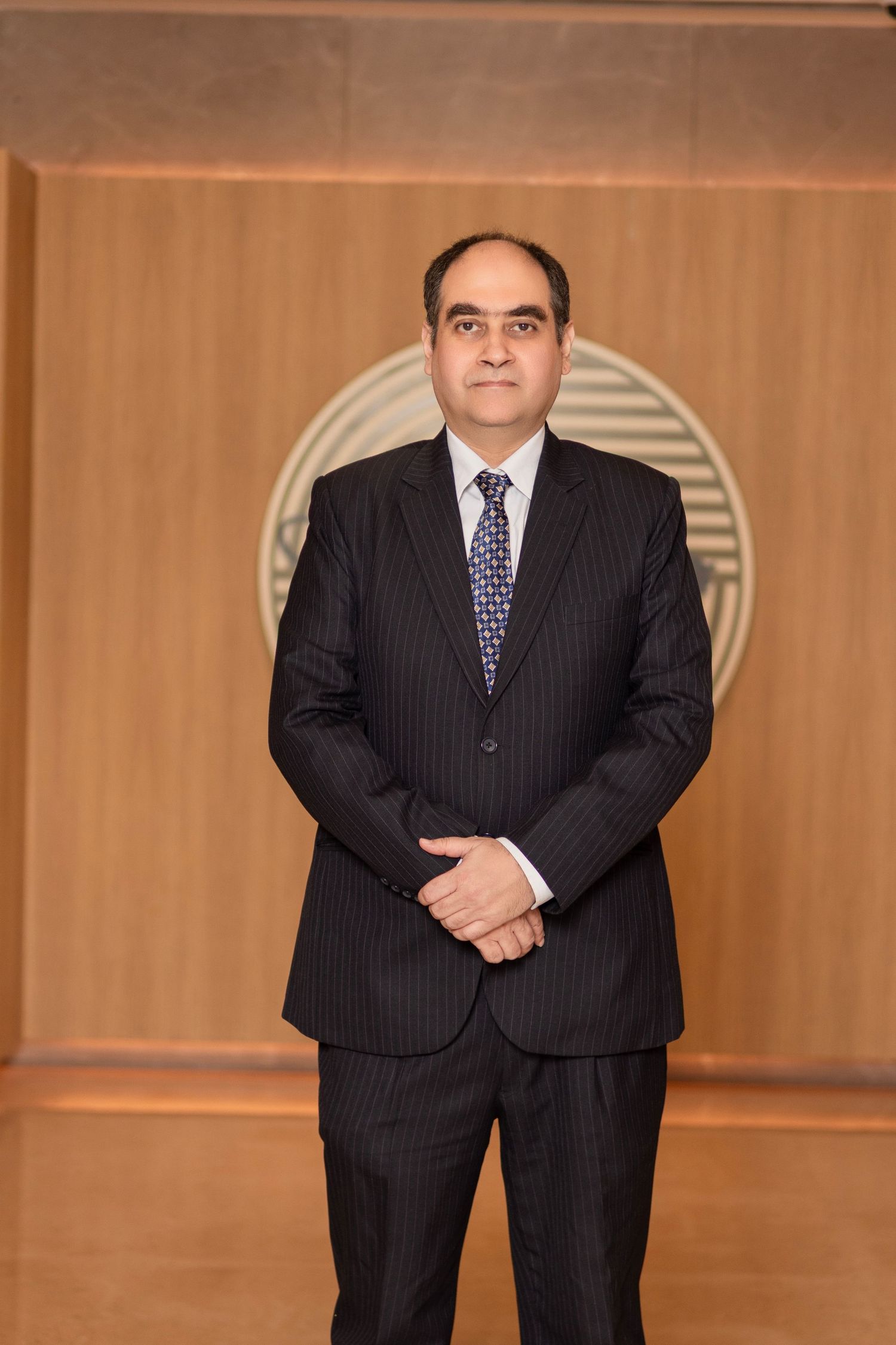 Professional in a pinstriped suit standing in front of a wood-paneled wall in a corporate setting.