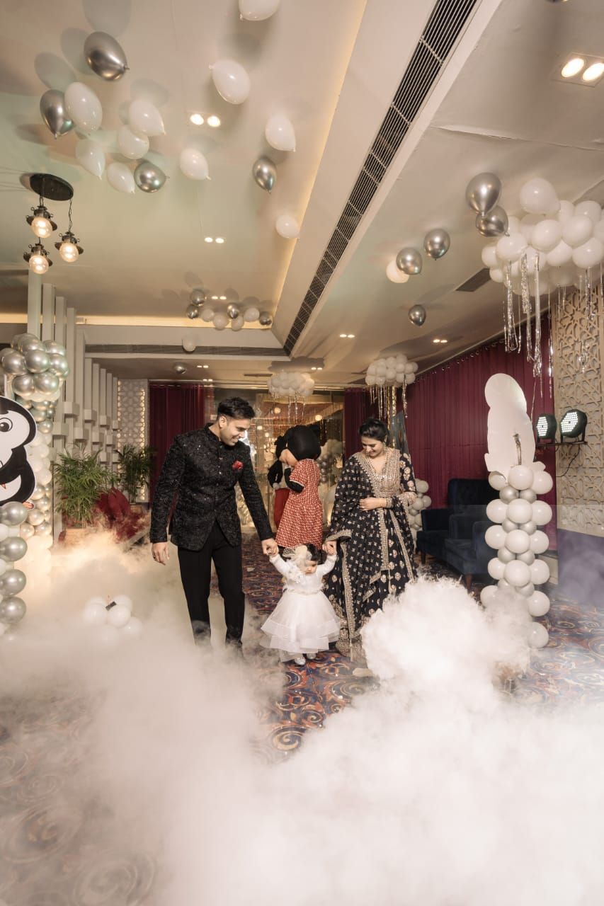 Family in elegant Indian attire walks through foggy venue with white balloon decor at a festive celebration.