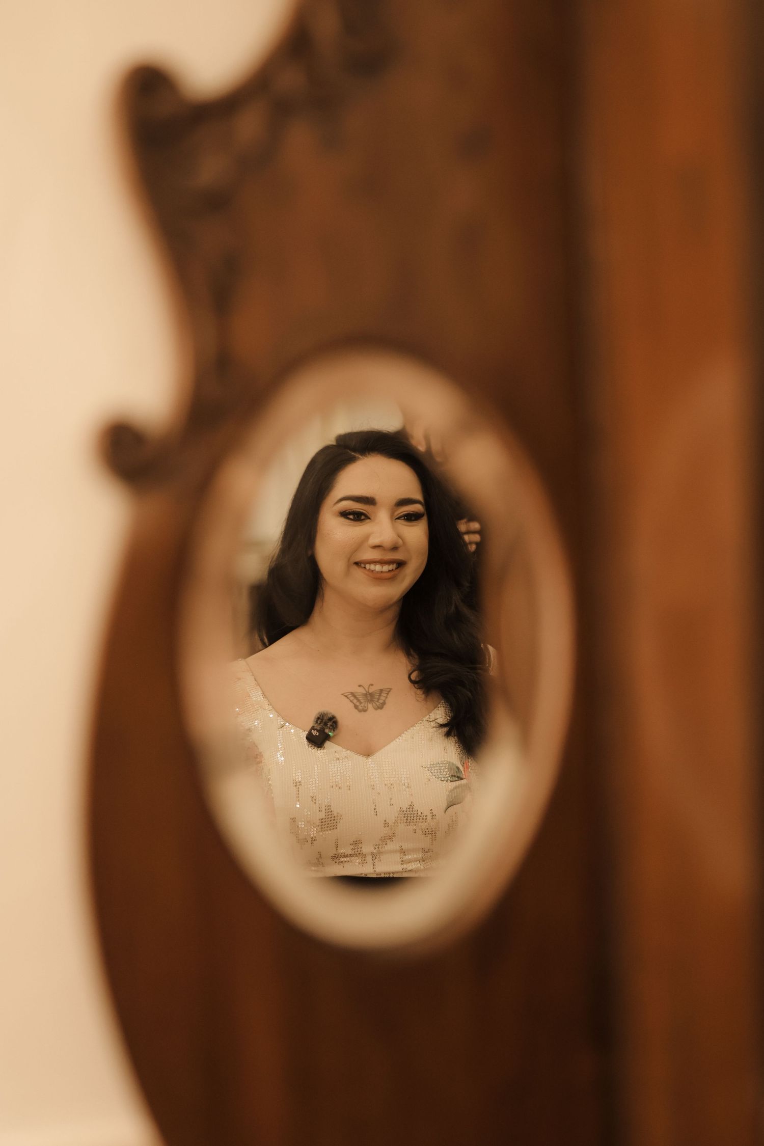 Reflection in vintage oval mirror shows a woman in white dress with dark hair and necklace in sepia tones.