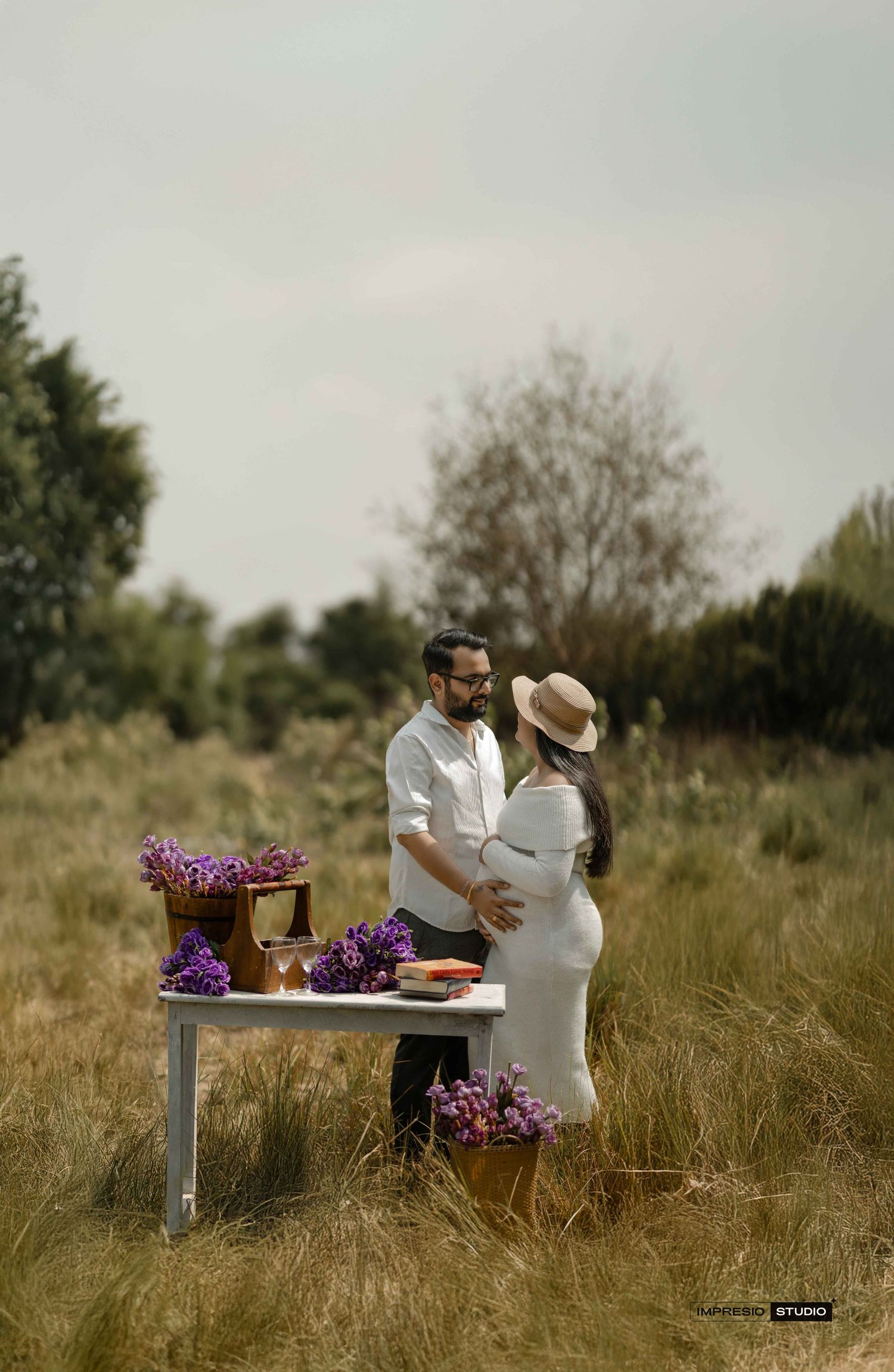 Couple sharing a tender moment outdoors at a rustic table adorned with purple flowers during a maternity photoshoot.