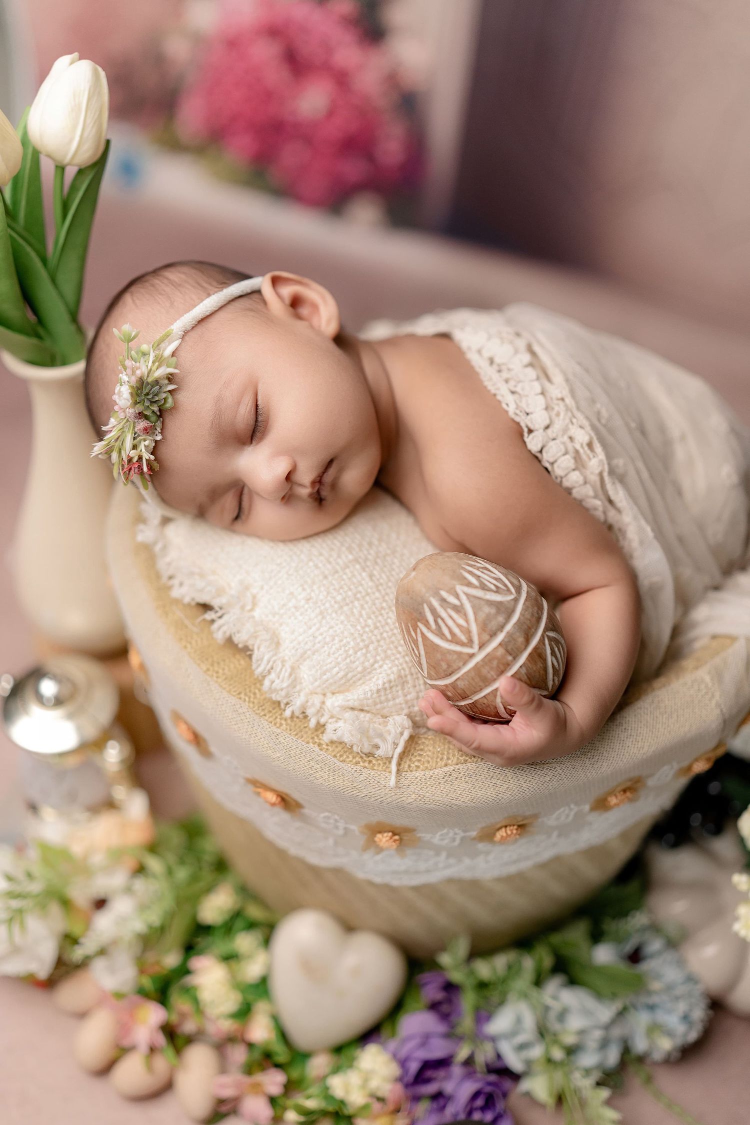 Peaceful newborn baby sleeping in a decorative basket surrounded by flowers and a floral headband.