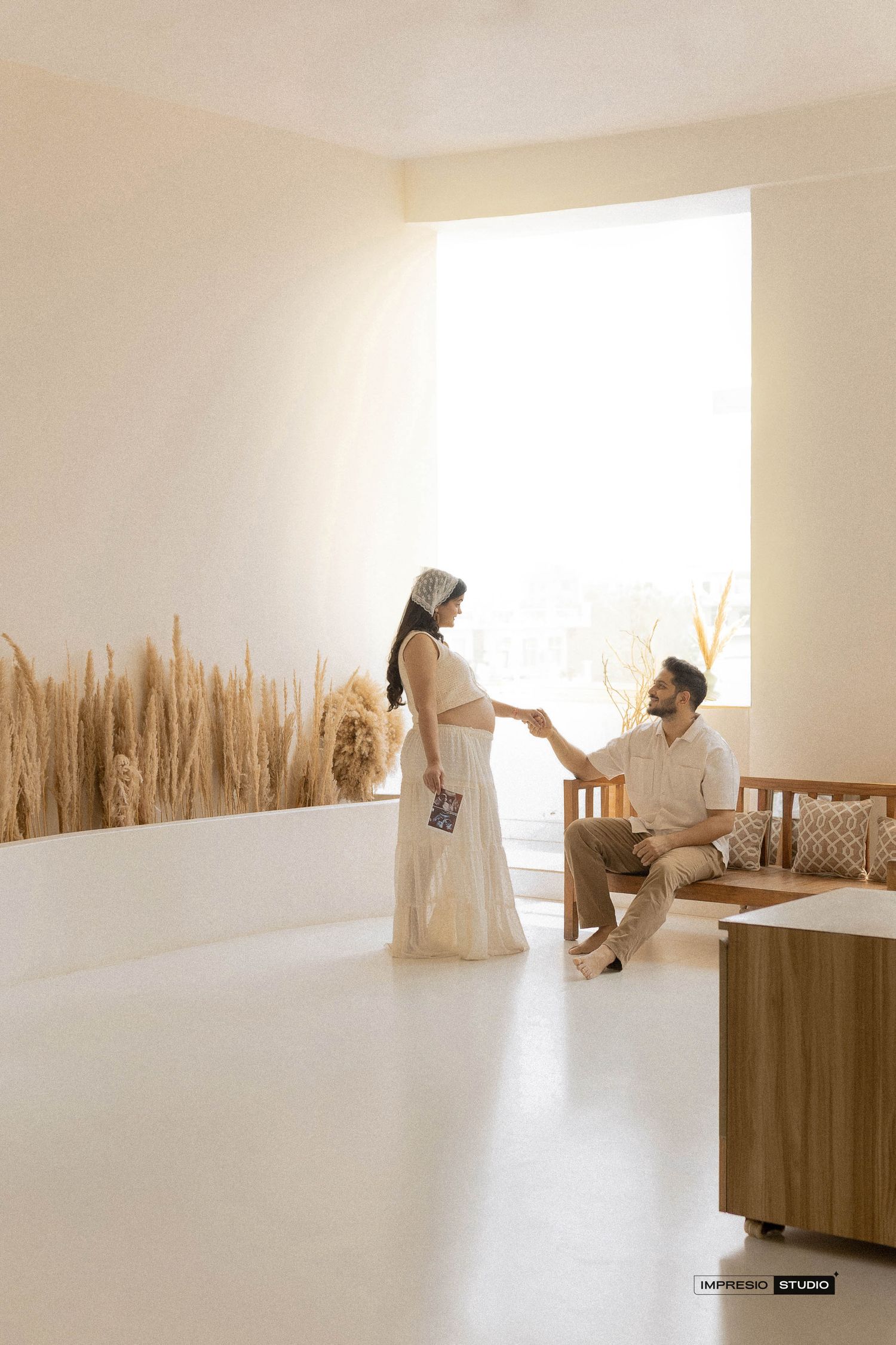 A couple shares a romantic moment in a minimalist beige room with dried pampas grass decor and warm natural light.