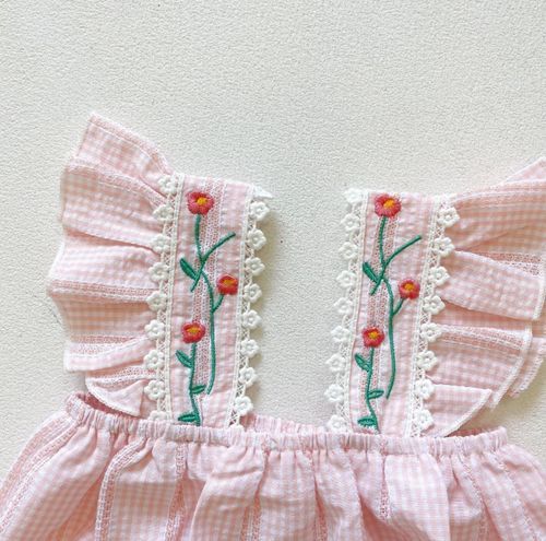 Pink gingham fabric with embroidered floral trim and ruffle details shown in close-up.