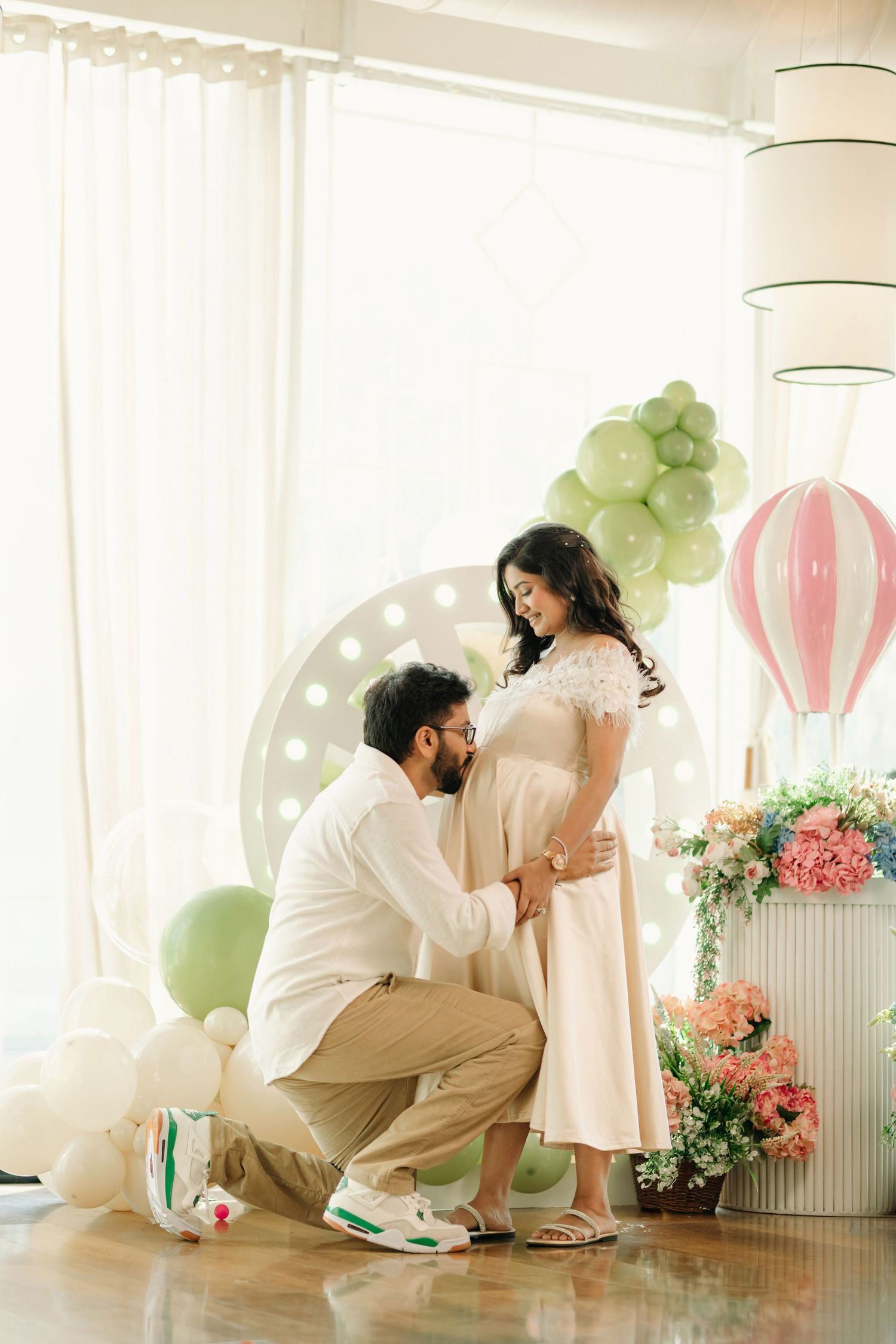 Couple sharing a tender maternity moment surrounded by pastel balloons and floral decor during an elegant baby shower photoshoot.