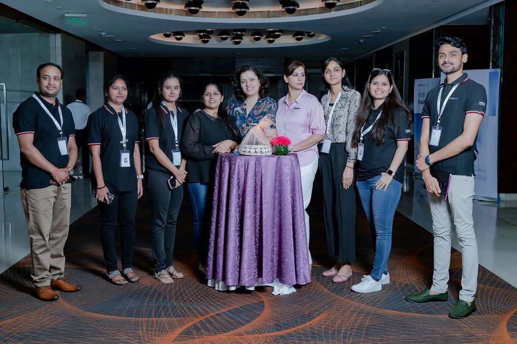 Group of nine professionals pose together at a corporate event with a woman in a purple outfit at center.