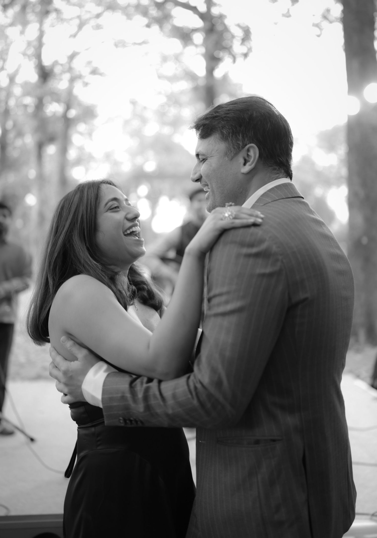Black and white photo of a couple dancing and laughing together outdoors at an evening event.