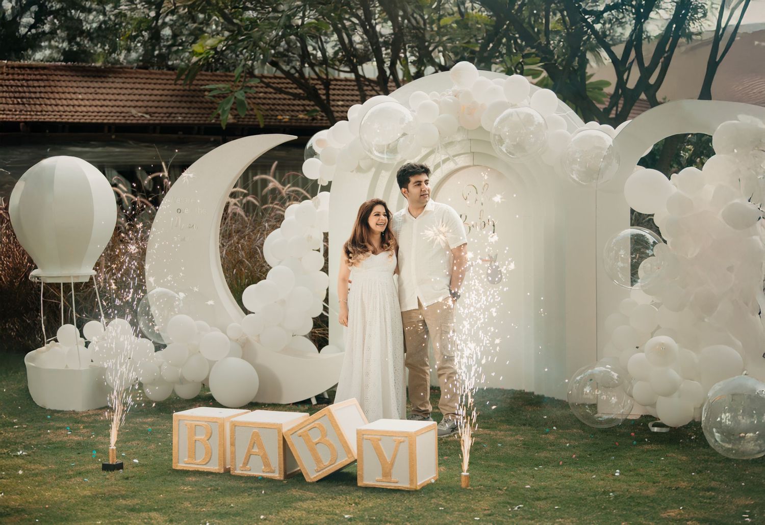 Couple poses under white balloon arch with moon decor and BABY letter blocks at outdoor baby shower.