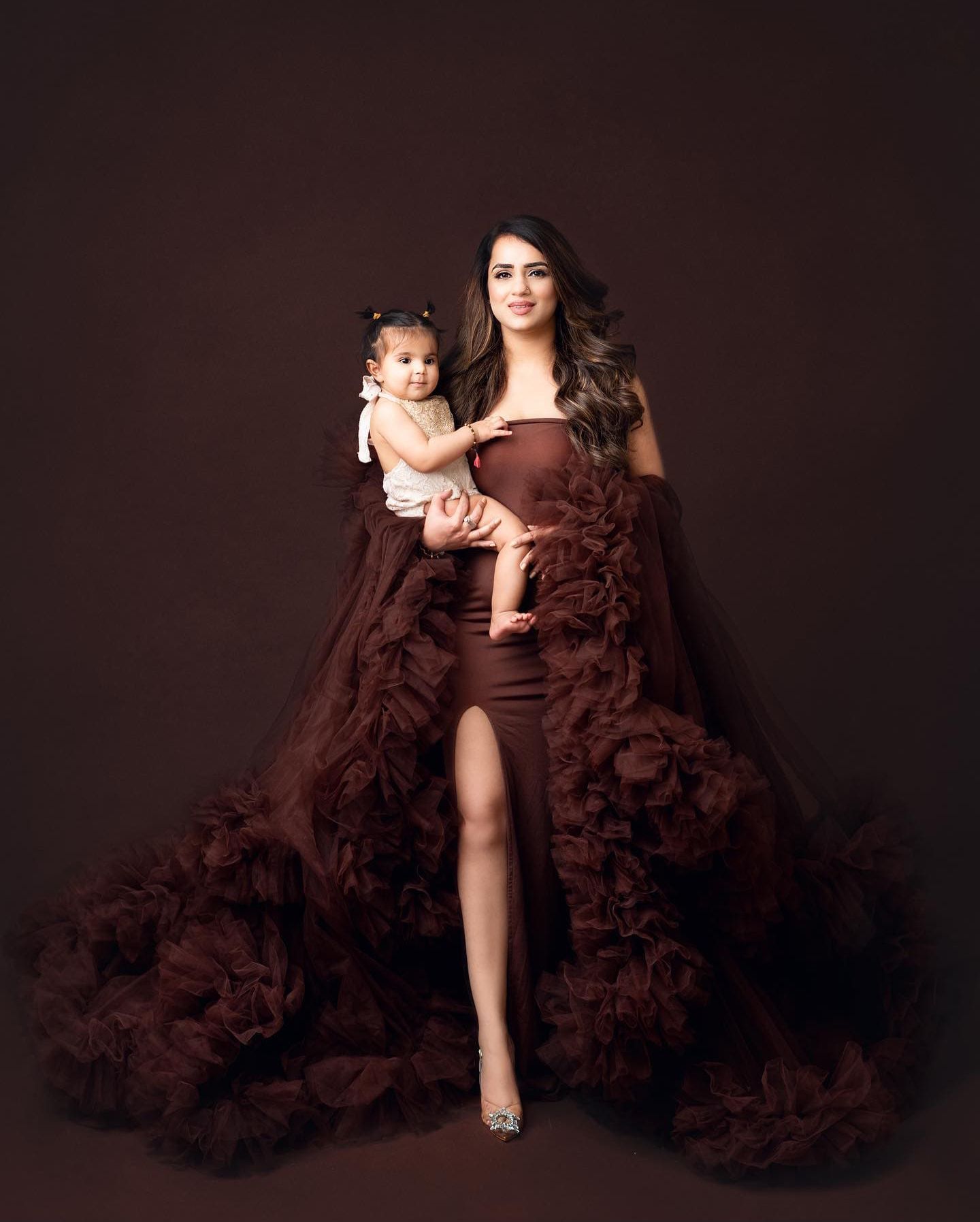 Elegant maternity portrait featuring a brown ruffled gown against dark background with matching outfits.