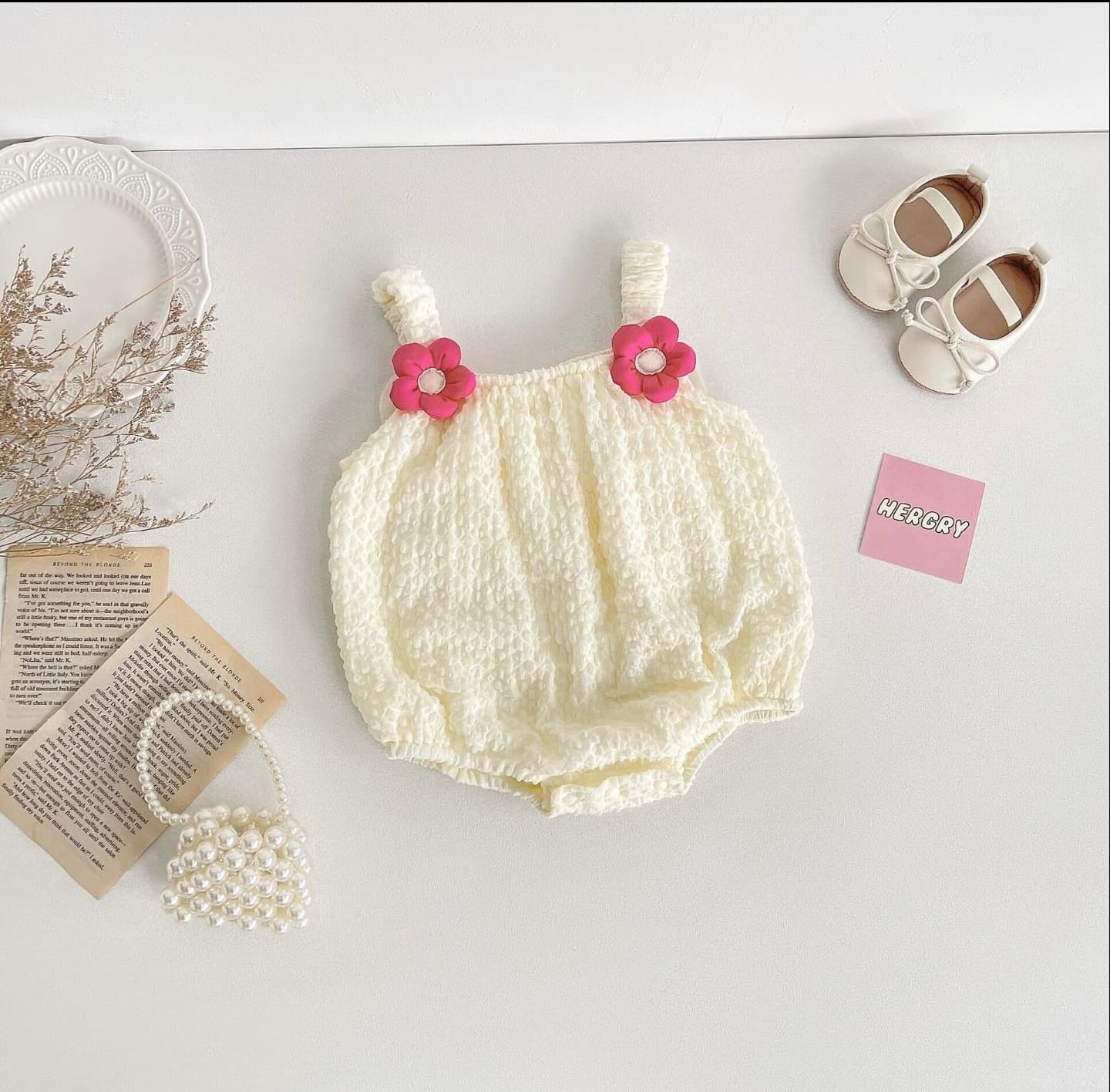 Vintage-inspired cream knit baby bloomers with delicate floral details laid flat on soft white backdrop.