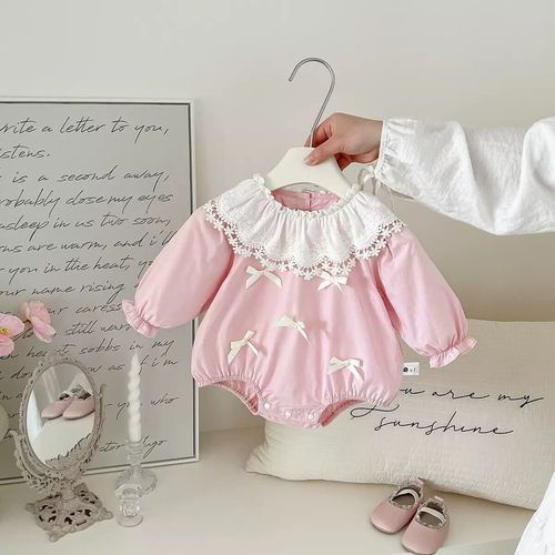 Pink and white vintage-style baby dress with lace collar displayed alongside antique letter and papers on white surface.