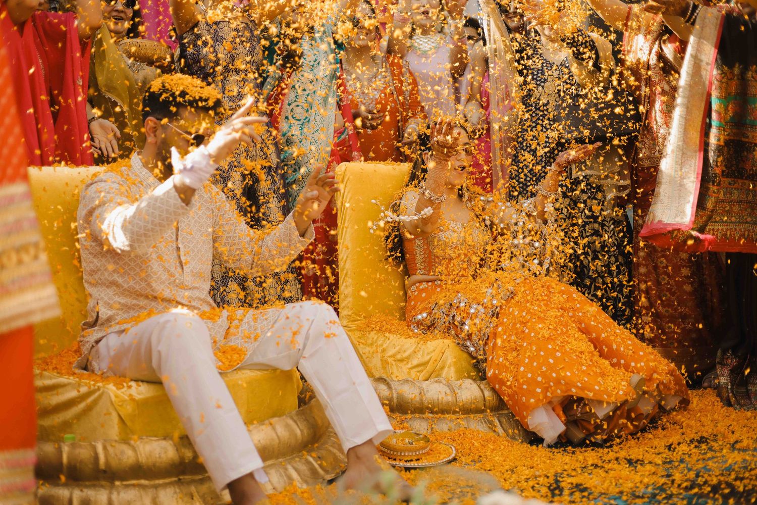 Couple celebrates vibrant Indian wedding ceremony with colorful flower petals raining down in joyful traditional ritual.