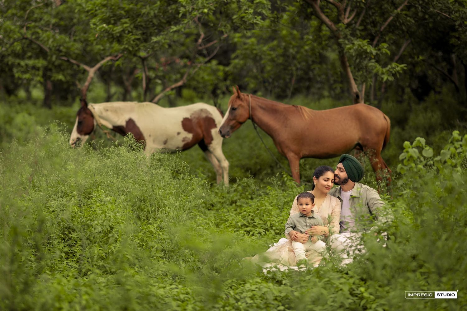 A couple sits in a meadow with horses grazing in the background on a summer day.